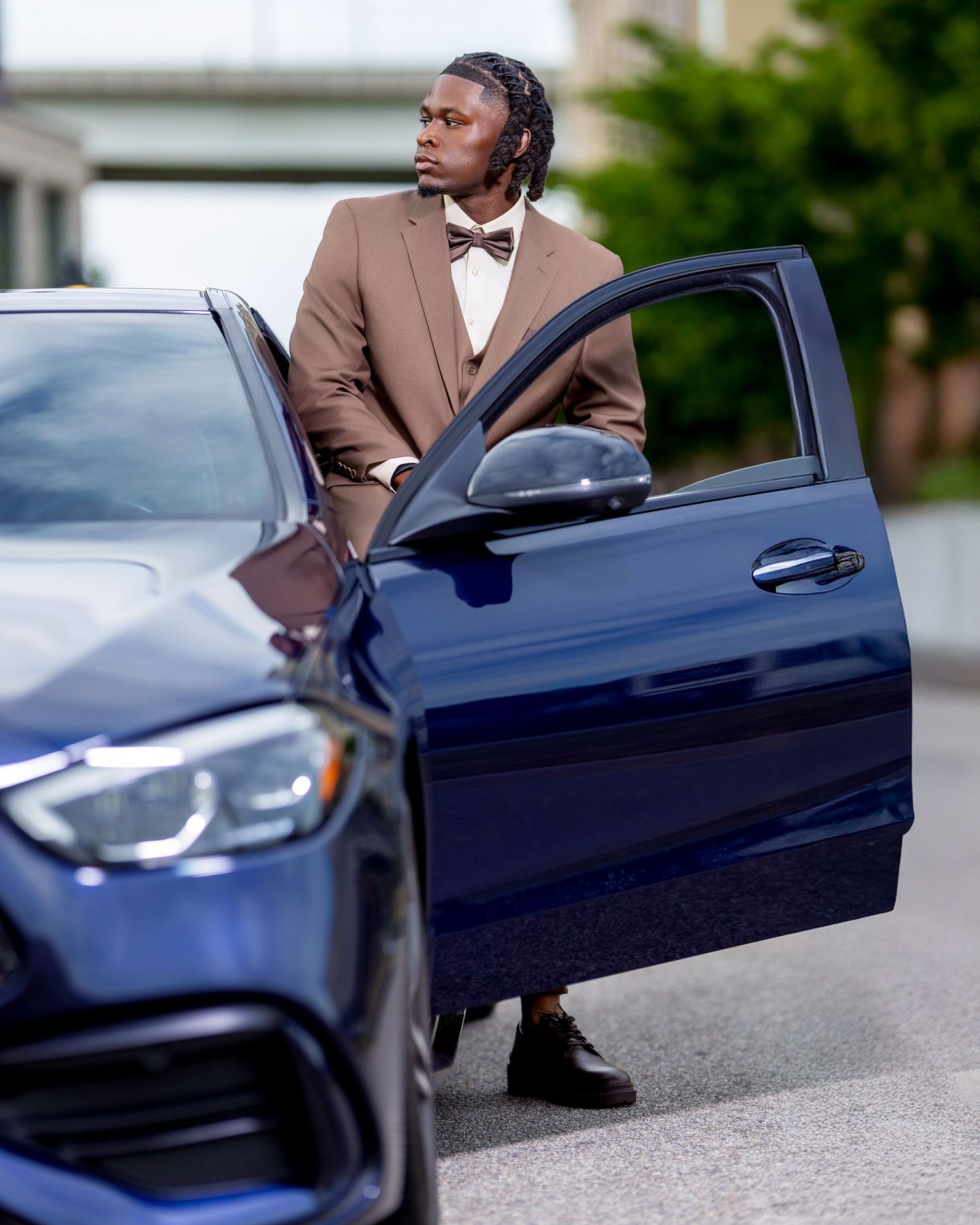 Fashionable man in tan suit with bow tie stepping out of blue Mercedes-Benz luxury car.