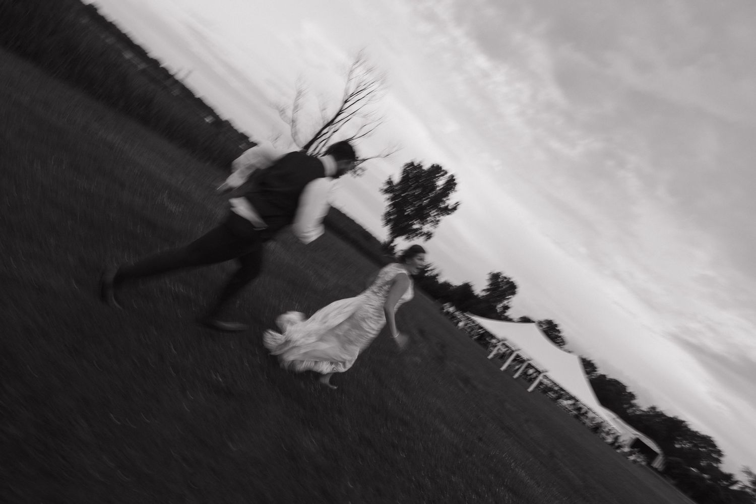 Black and white photo of bride and groom running across an open field on their wedding day.