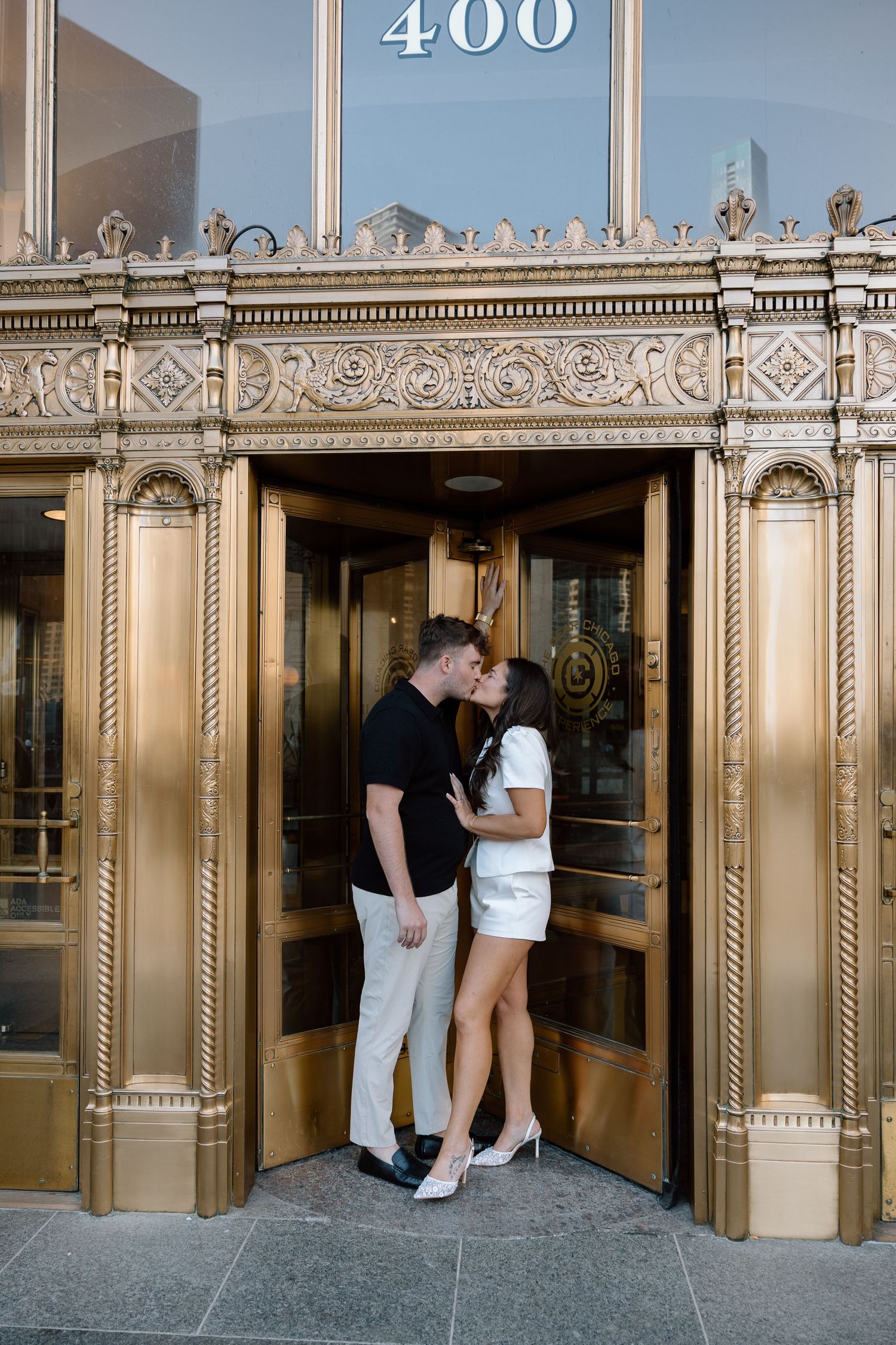 Couple sharing a romantic kiss in front of elegant gold revolving doors at 400 building entrance.