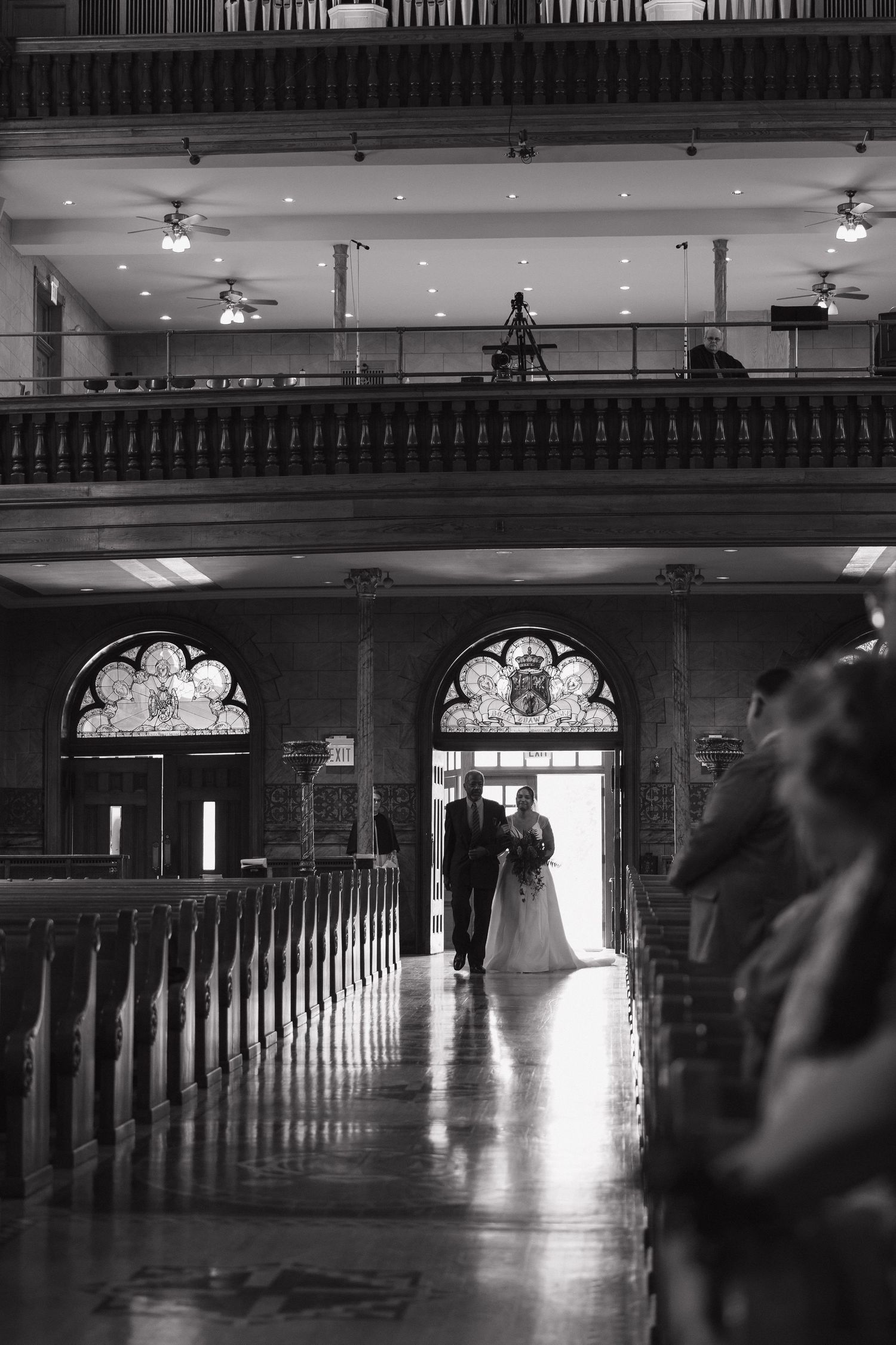 Black and white photo of a bride and groom walking down the aisle of an elegant church with stained glass windows.