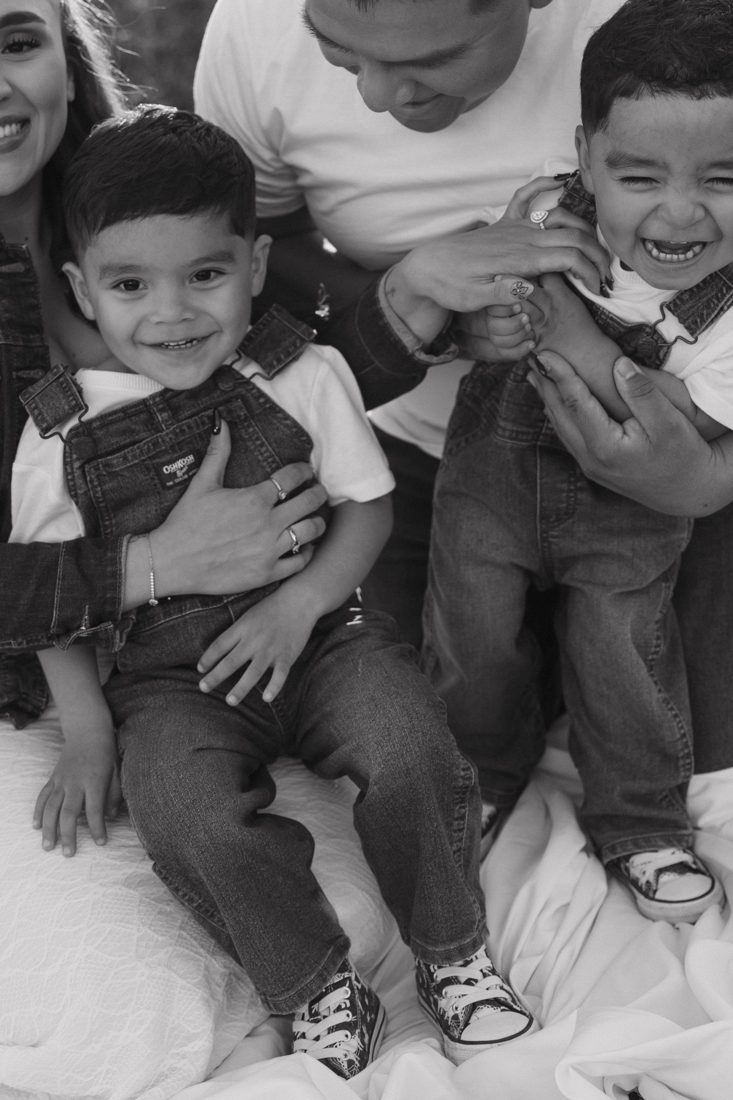 Black and white portrait of two young brothers in denim overalls smiling with their parents.