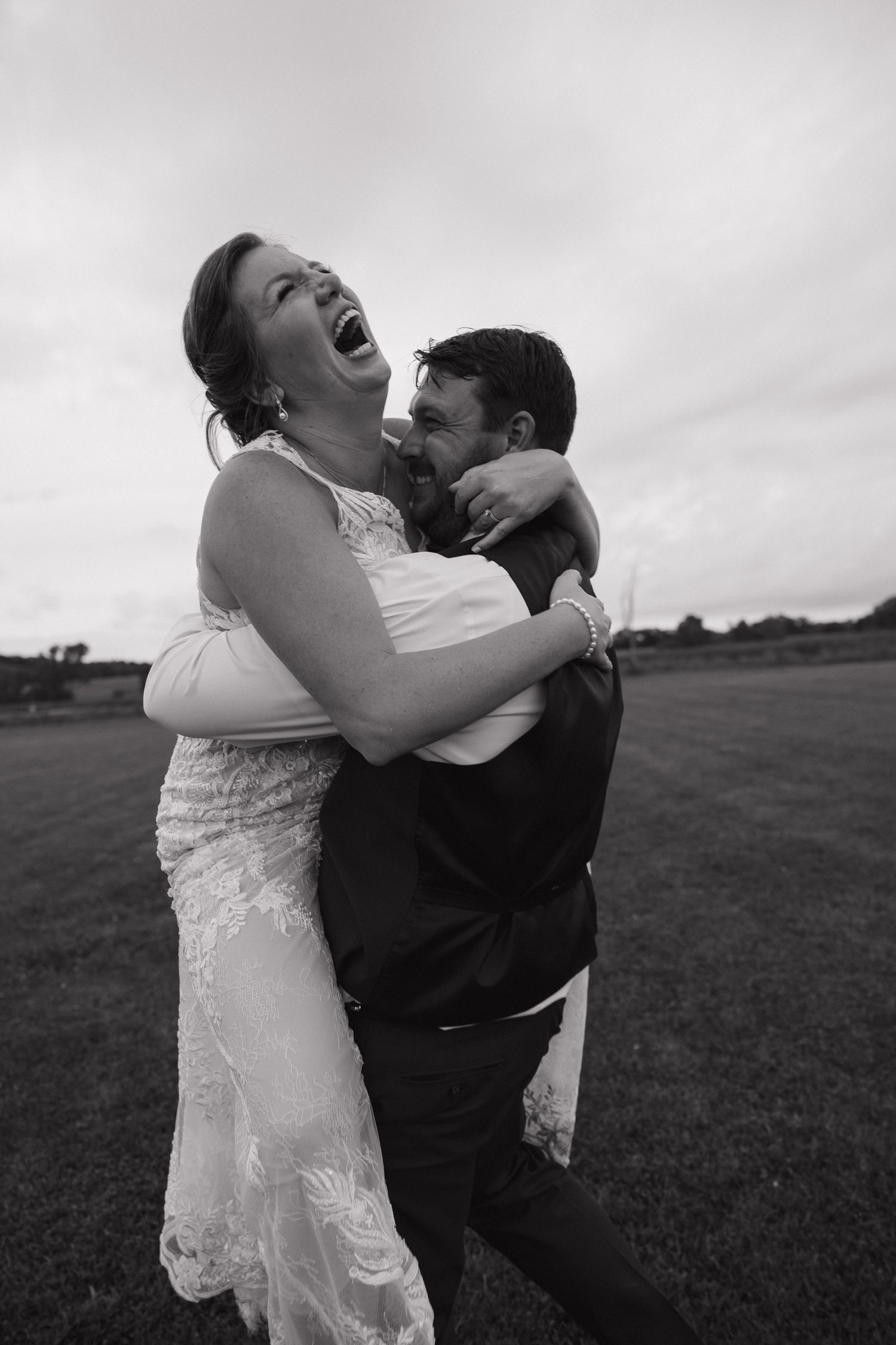 Black and white photo of bride and groom laughing joyfully while embracing outdoors on their wedding day.