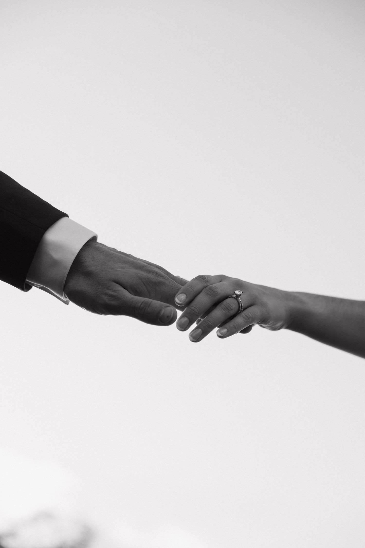Black and white photo of a couple holding hands, with a diamond engagement ring visible on the woman's finger.