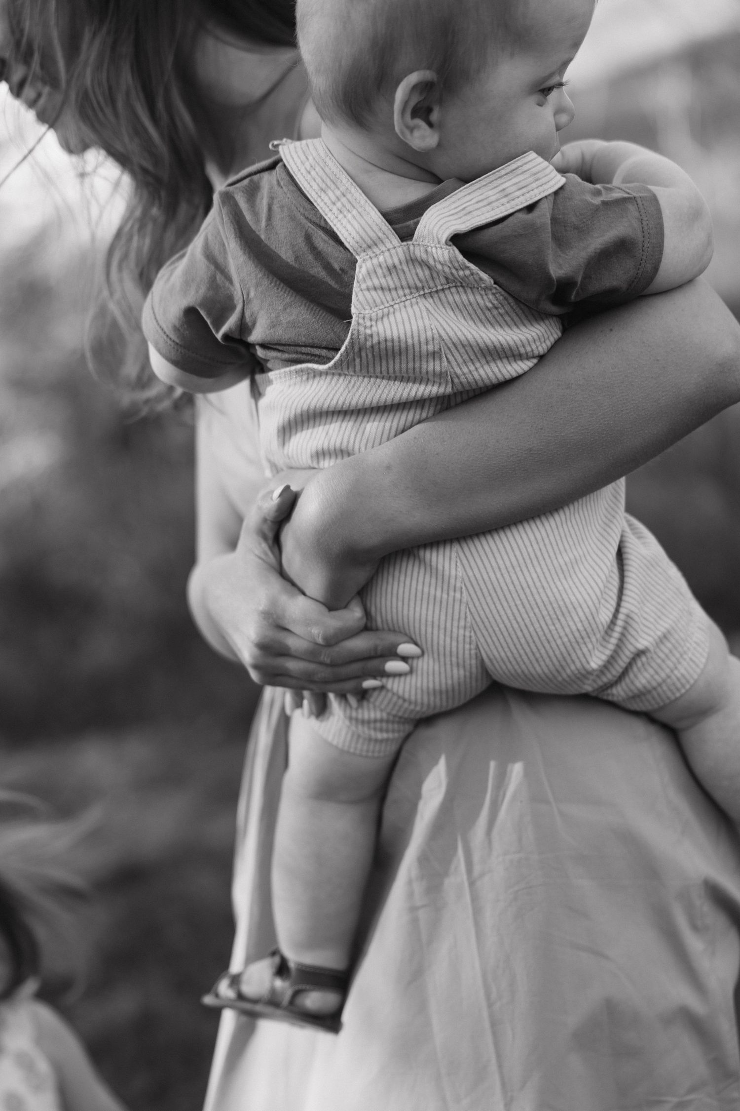 Black and white close-up of a mother tenderly holding her baby in a striped romper outdoors.