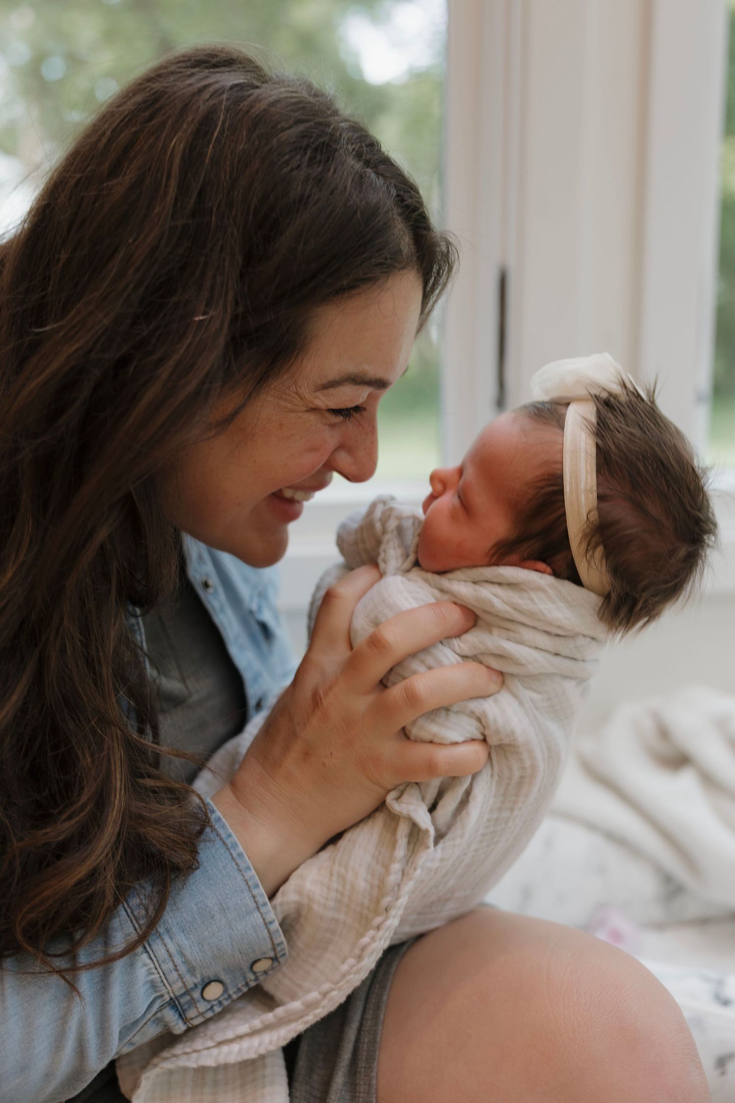Smiling brunette mother gazing lovingly at her newborn baby wrapped in a soft blanket.