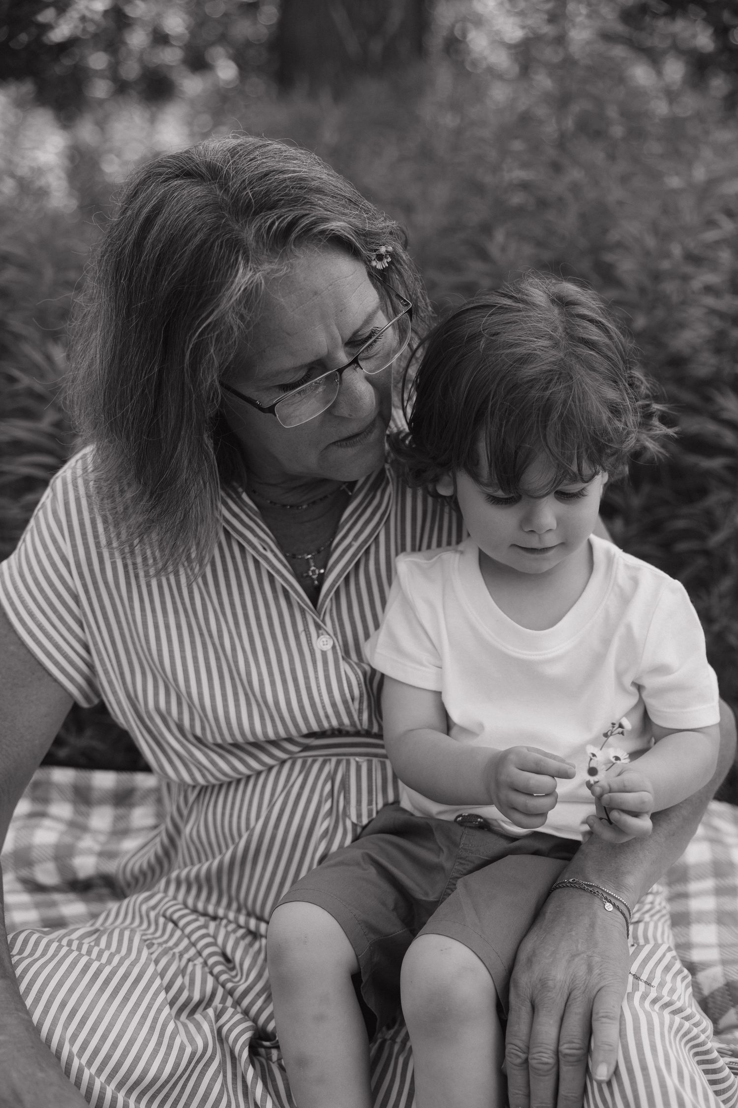 Black and white portrait of grandmother with glasses sitting outdoors holding young grandchild on lap.