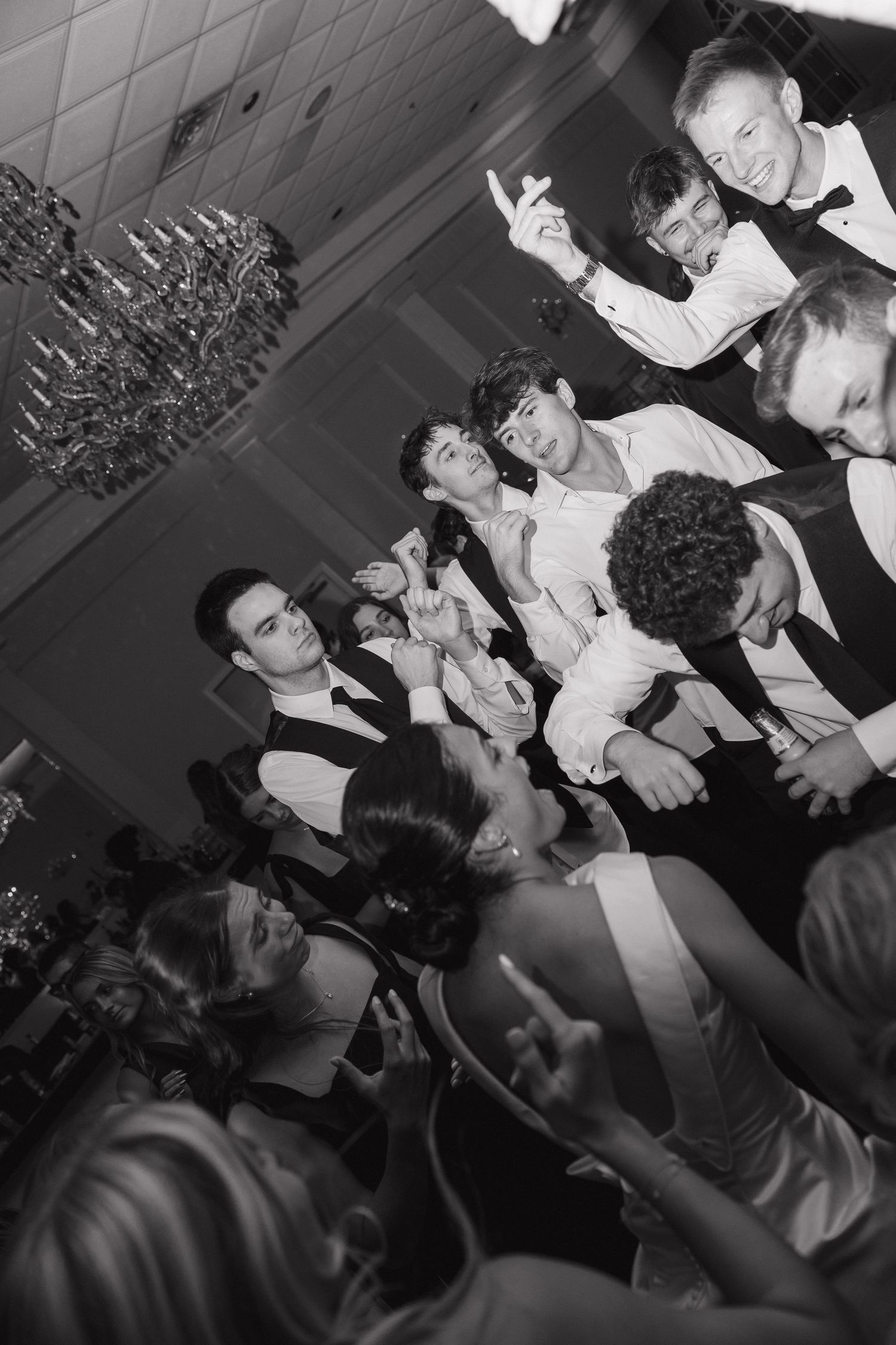 Black and white photo of elegantly dressed guests dancing and celebrating at a formal wedding reception party.