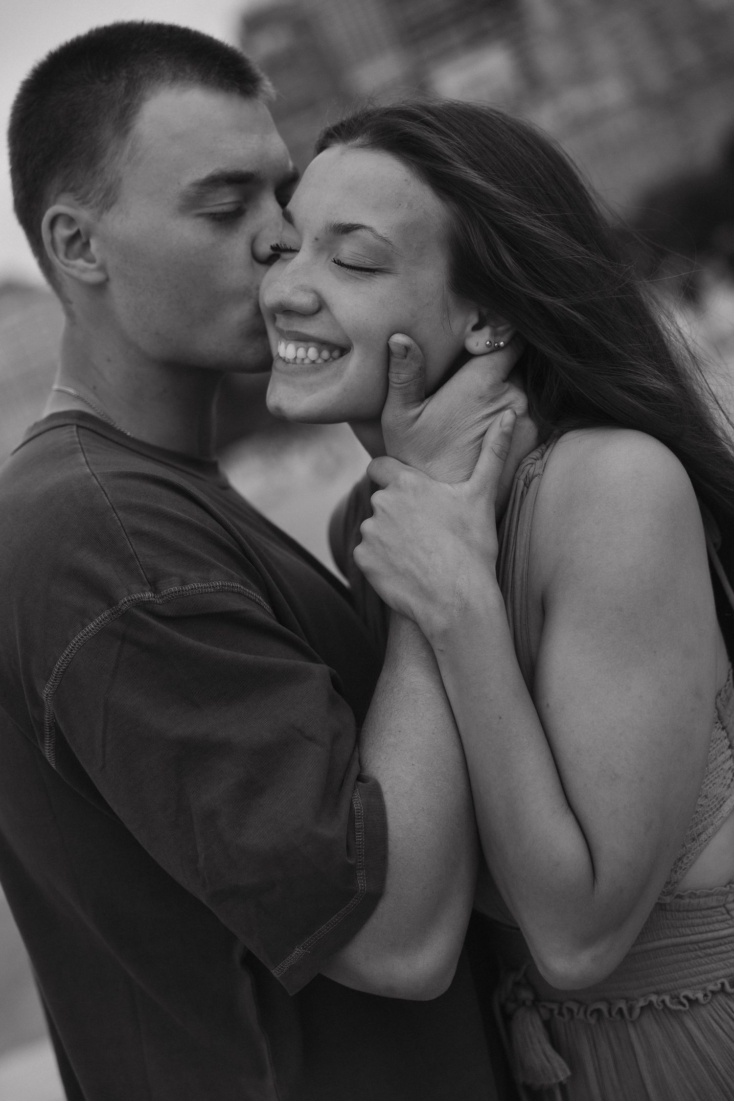 Black and white romantic photo of man kissing smiling woman on the cheek outdoors.