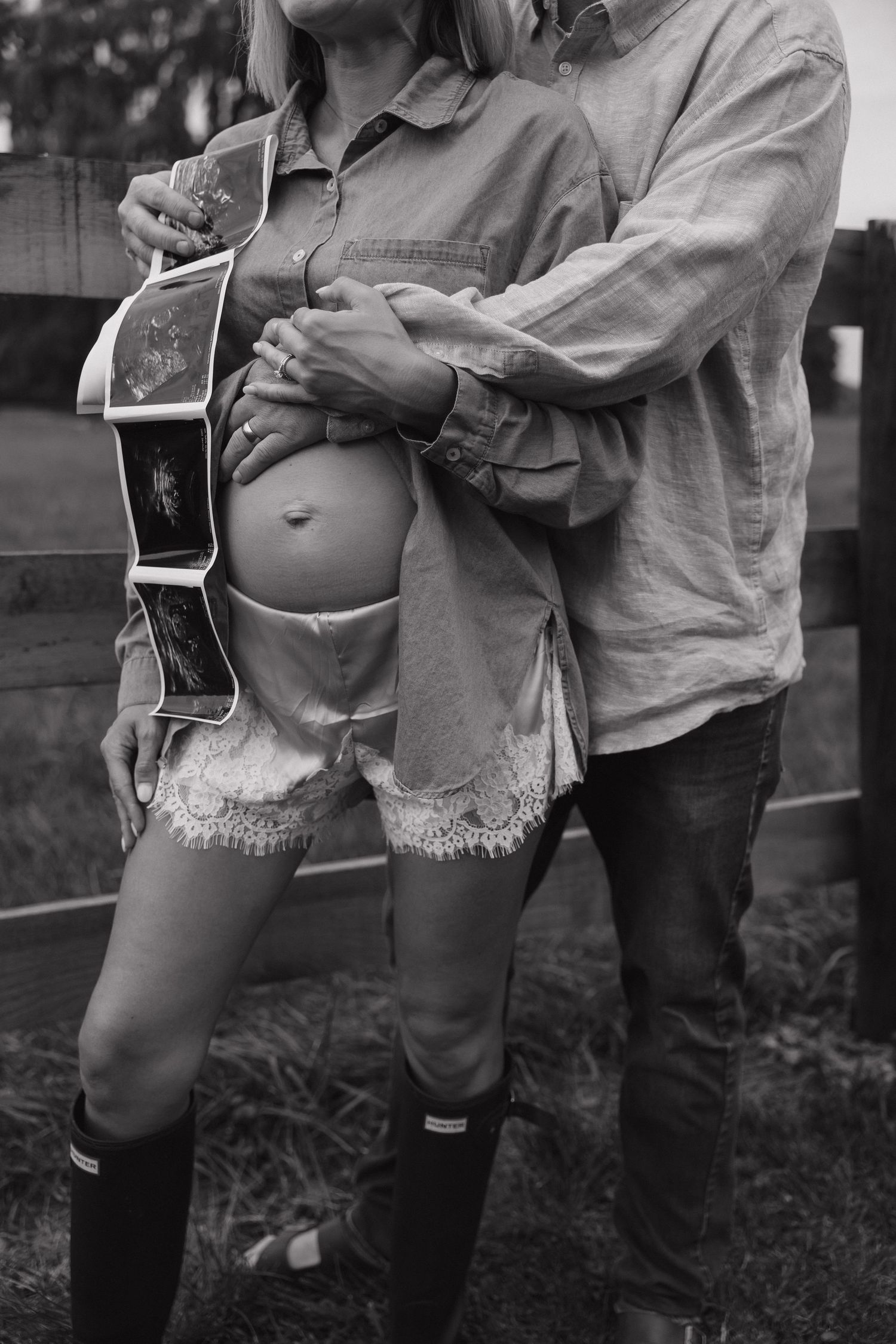 Black and white photo of couple embracing showing pregnant belly with ultrasound photos.