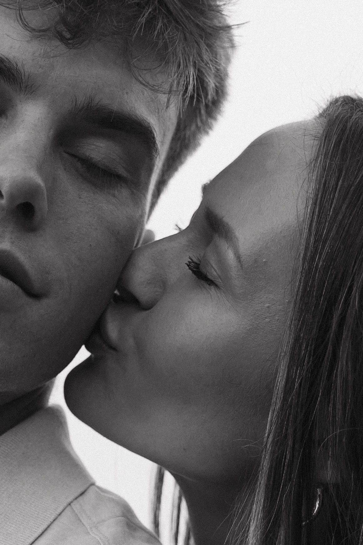 Close-up black and white photo of young couple sharing a tender kiss.