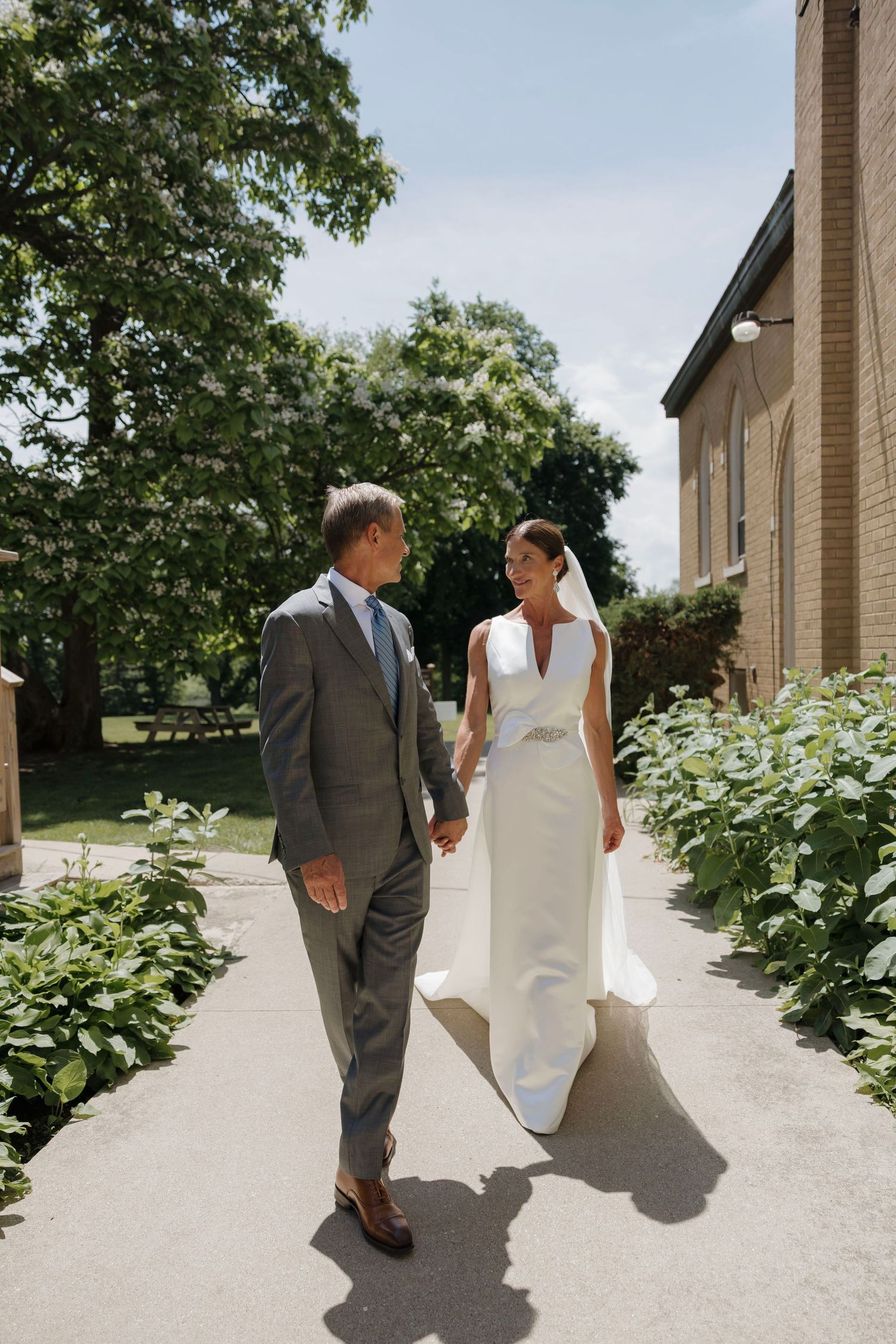 Bride and groom holding hands walking outside church on sunny wedding day.