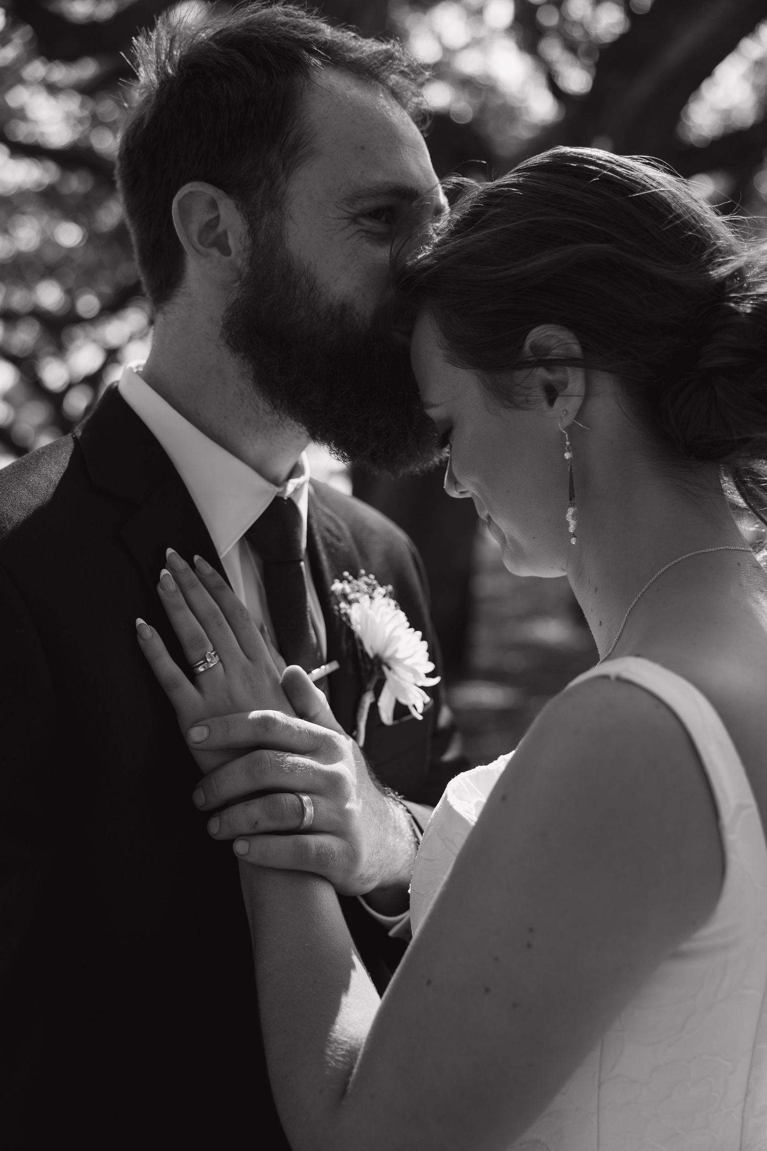 Black and white wedding photo of bearded groom and bride sharing intimate moment, bride showing ring.