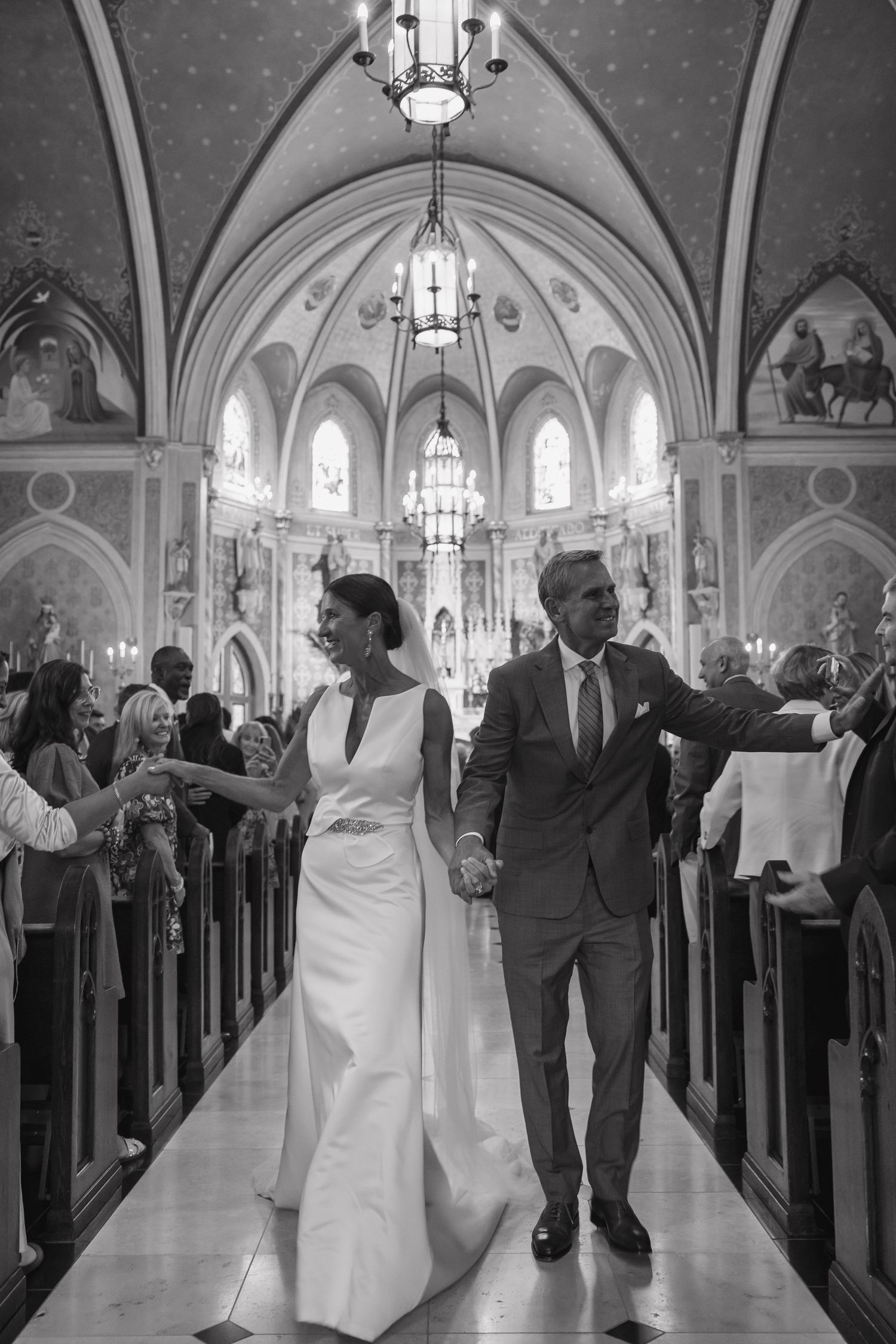 Black and white photo of newlyweds walking down church aisle after wedding ceremony.