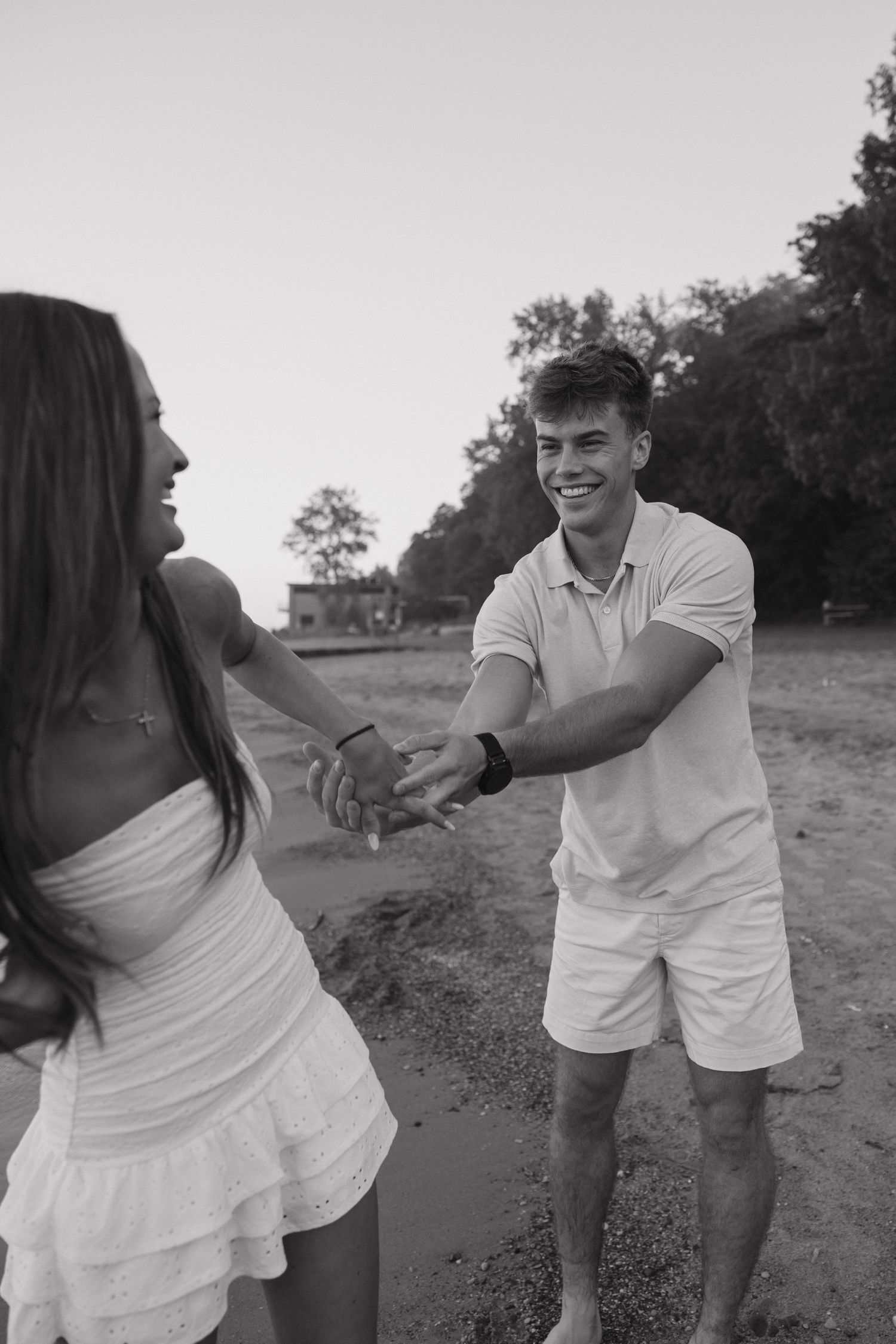Black and white photo of joyful couple holding hands and dancing on a sandy beach at sunset.