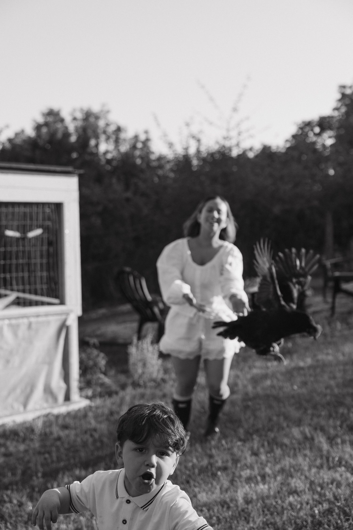 Black and white photo of a startled mother and child reacting to a flying chicken in backyard.