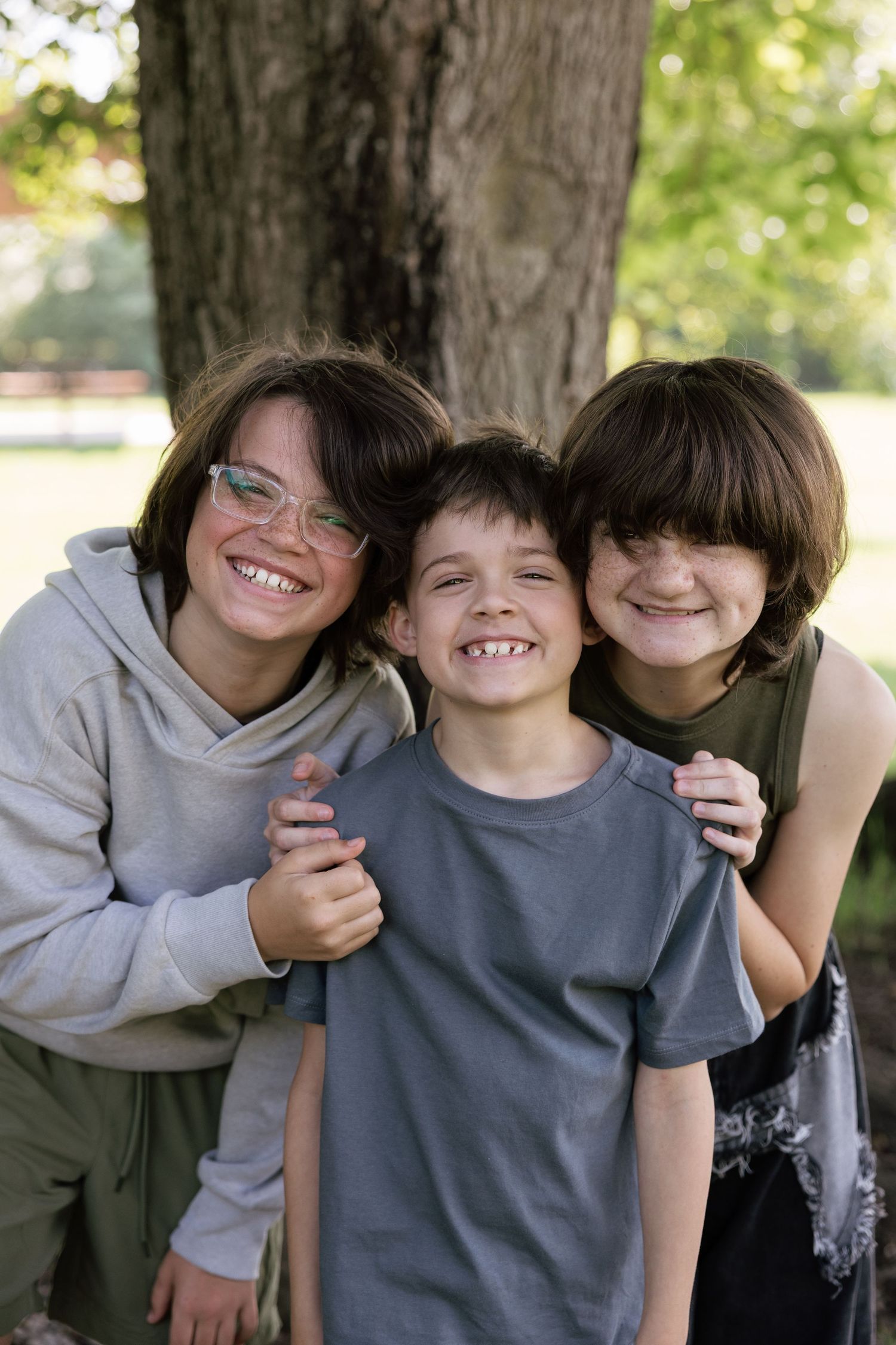 Three happy young brothers hugging and smiling together in front of a large tree.