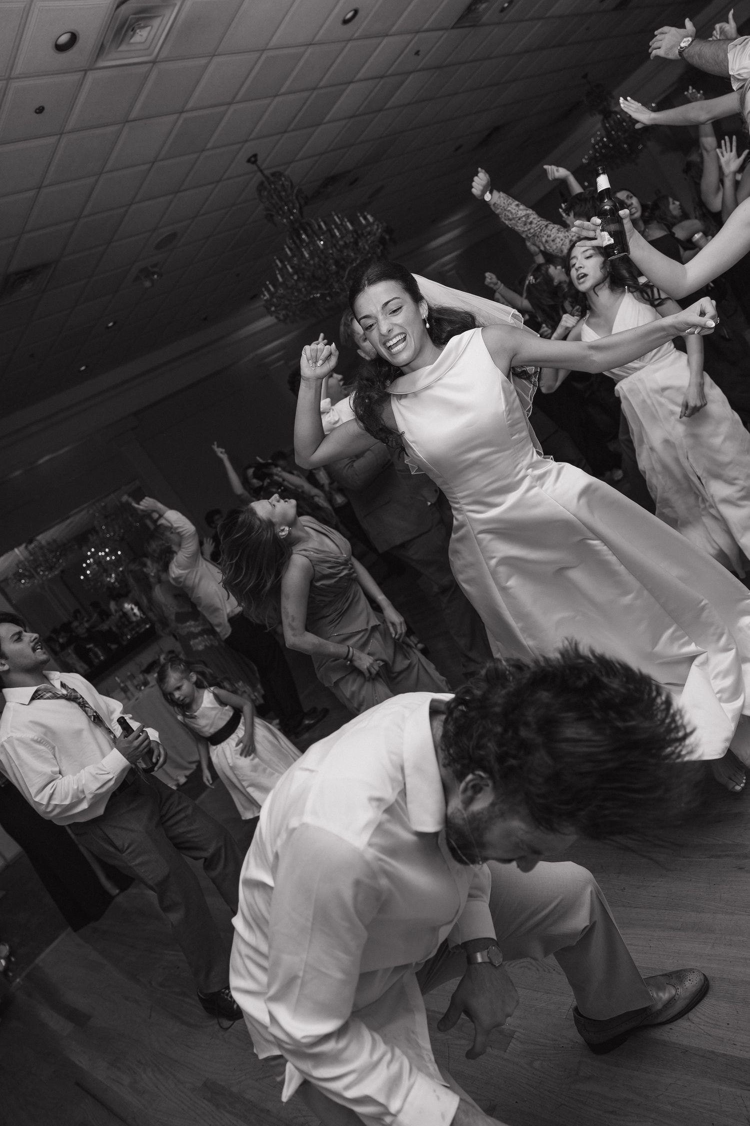 Black and white photo of joyful wedding guests dancing energetically at a lively reception celebration.