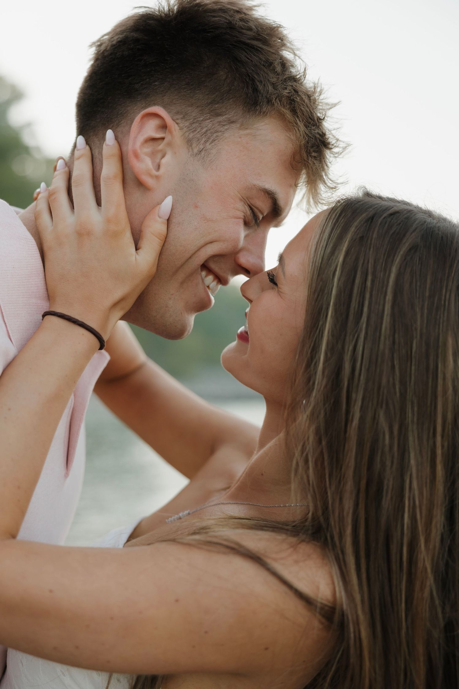 Smiling couple leaning in for a kiss outdoors, woman holding mans face tenderly in her hands.