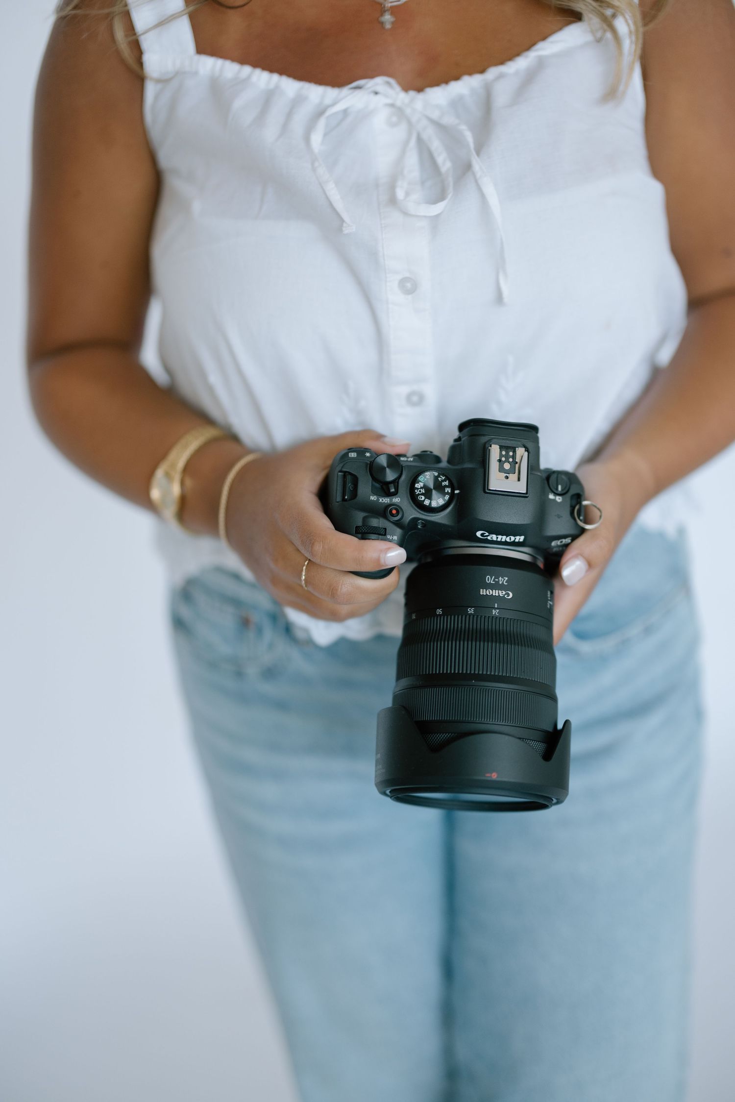 Woman in white top and jeans holding a Canon DSLR camera with zoom lens.