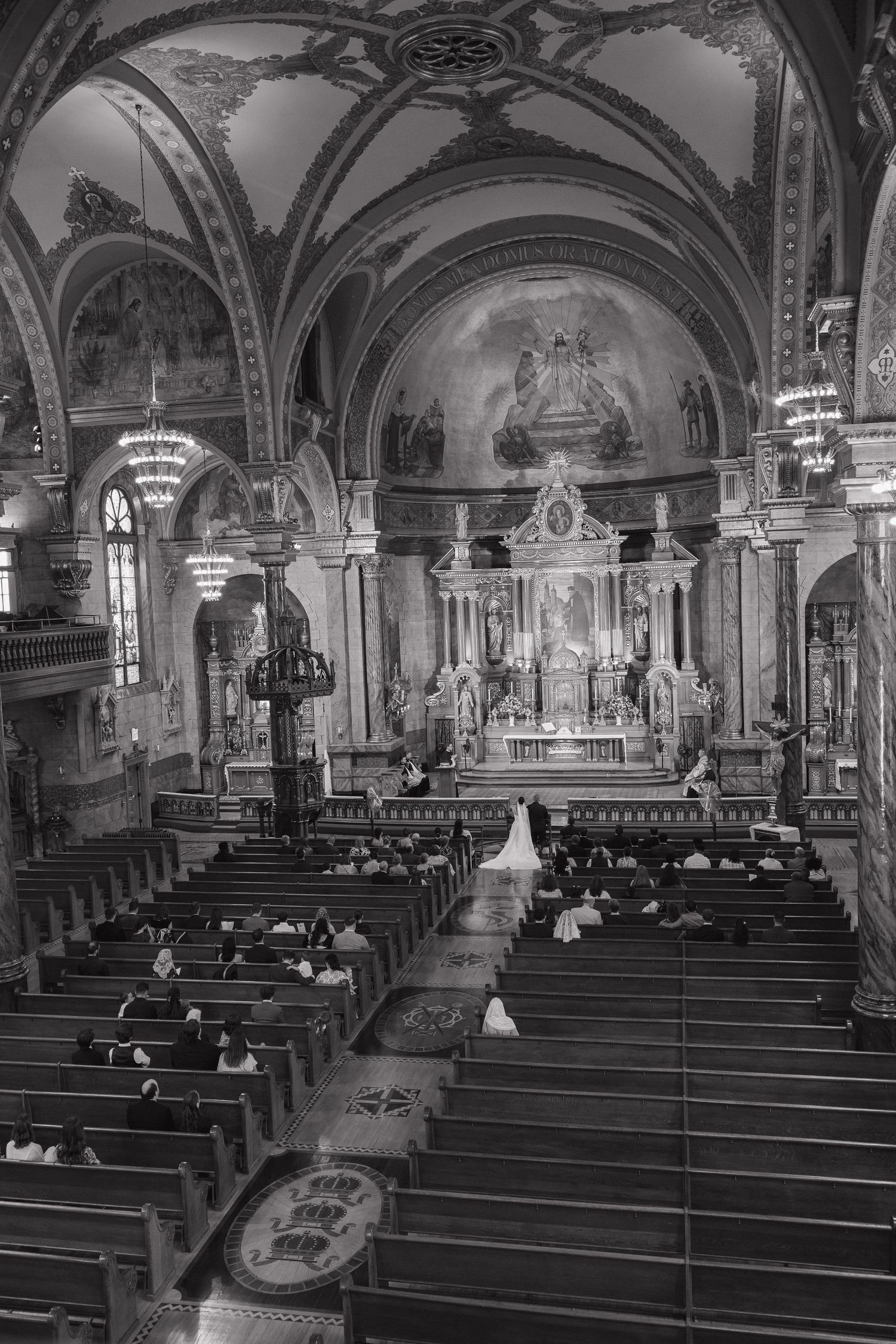 Black and white photo of a wedding ceremony inside an ornate Catholic church with vaulted ceilings and elaborate altar.