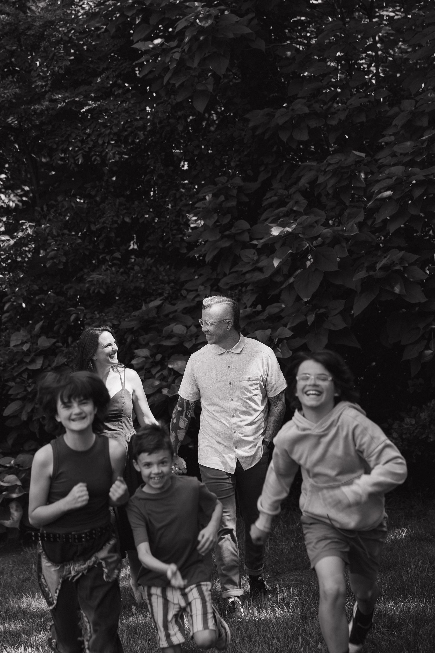 Black and white family photo of parents and three children running and laughing in a lush garden.