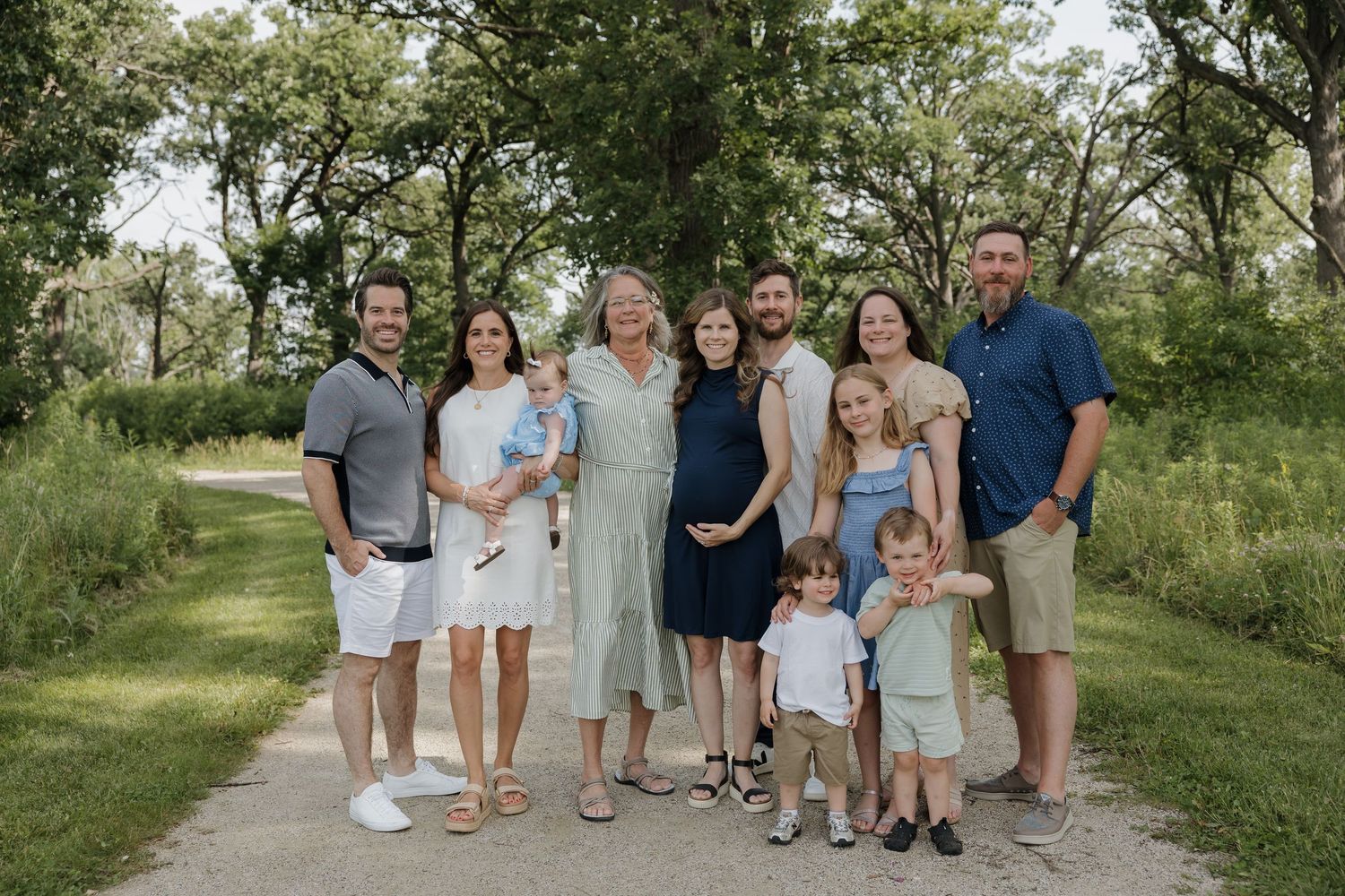 Large family group portrait on a scenic tree-lined path during a summer outdoor photo session.