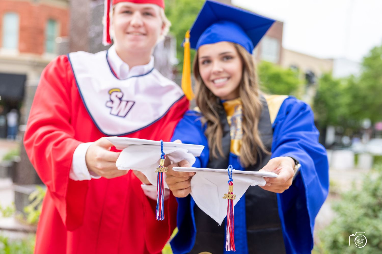 Graduates in red and blue caps and gowns holding diplomas during commencement ceremony.