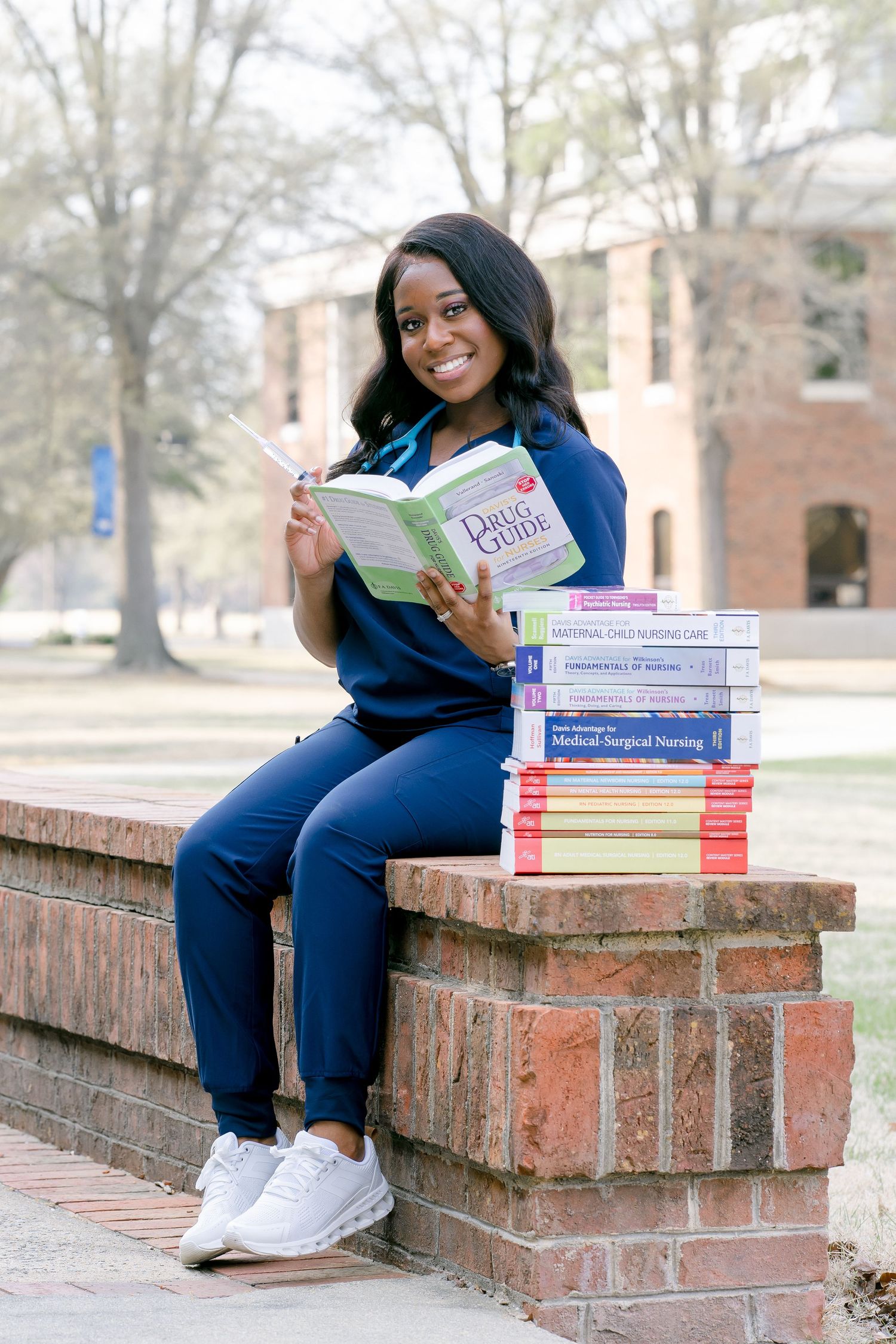 A person in navy scrubs sits on brick steps with medical textbooks and study materials beside them.