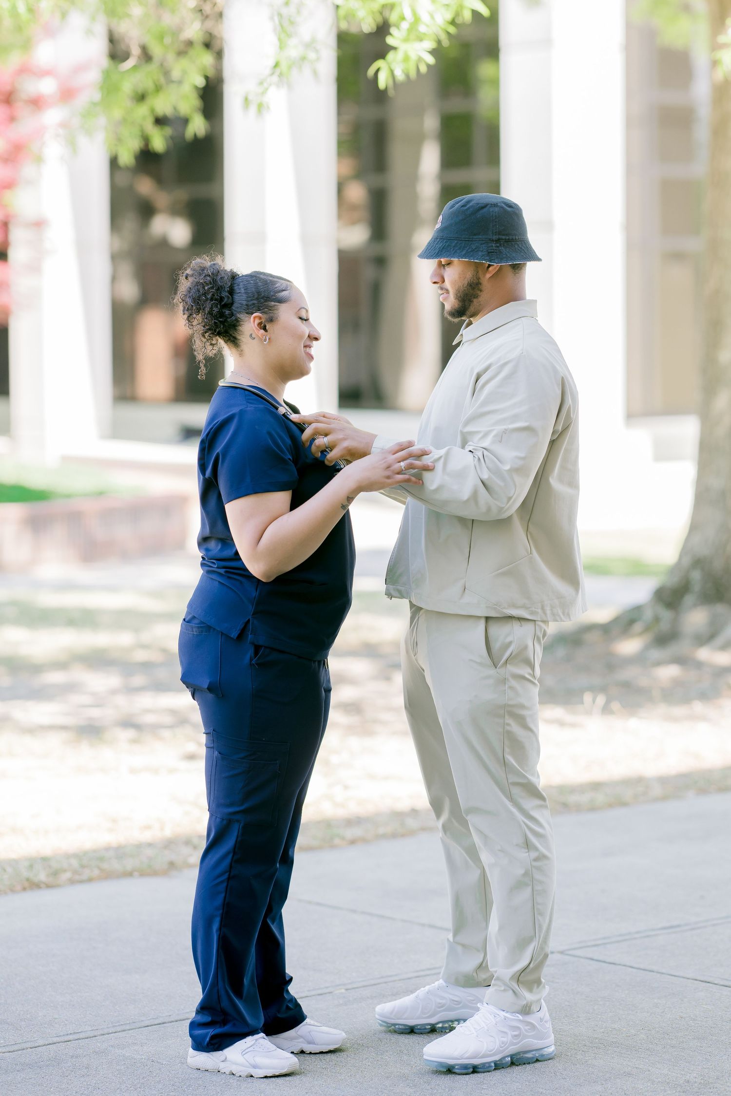 A woman in navy scrubs and a man in beige outfit face each other outdoors, engaged in a warm conversation.