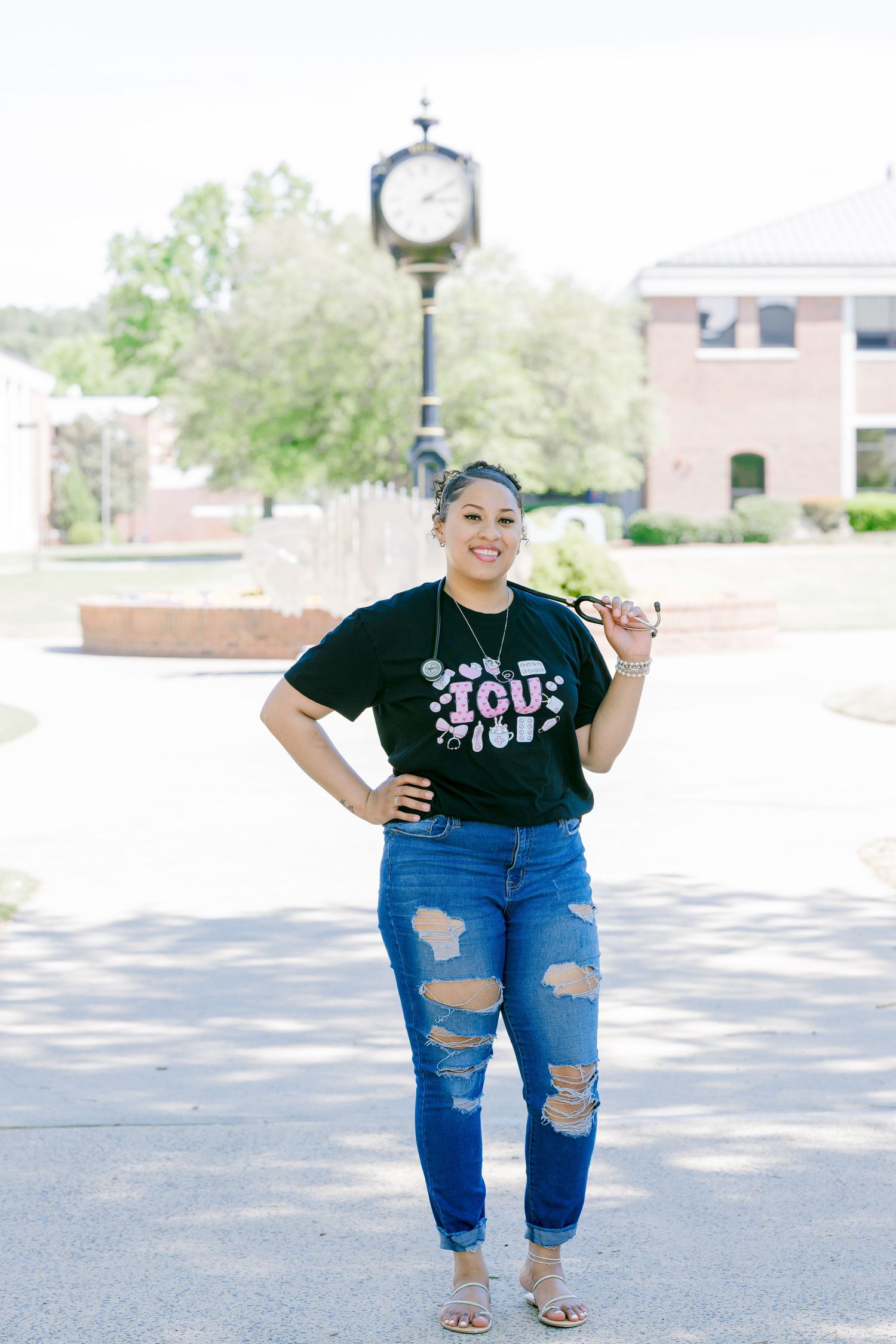 Young woman in black graphic tee and ripped jeans smiling outdoors near a campus clock tower.