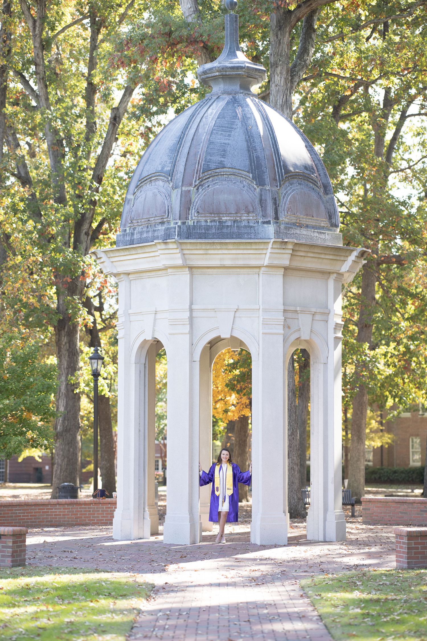 White classical domed gazebos line a brick pathway surrounded by autumn trees on a college campus.