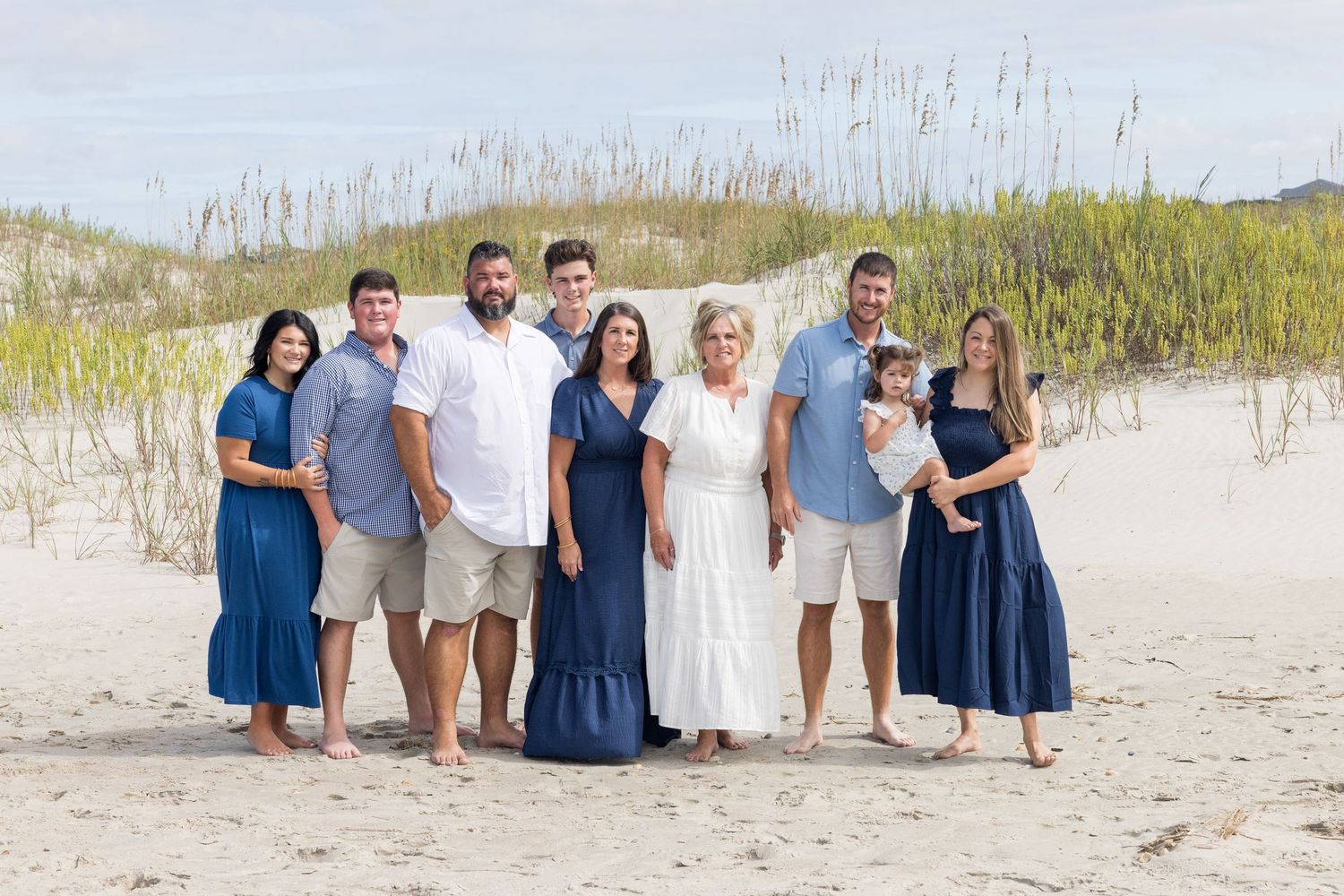 Family group photo session on a sandy beach with everyone wearing blue and white coordinated outfits.
