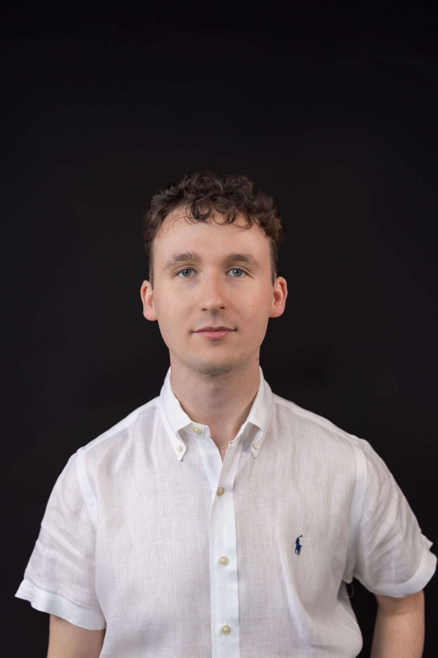 Portrait against black background wearing white polo shirt with small logo.