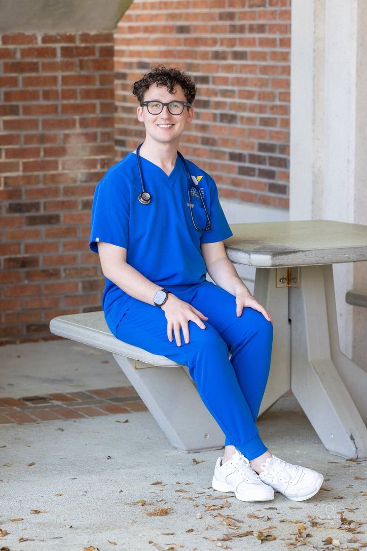 Someone in blue medical scrubs sits on a white bench against a brick wall.