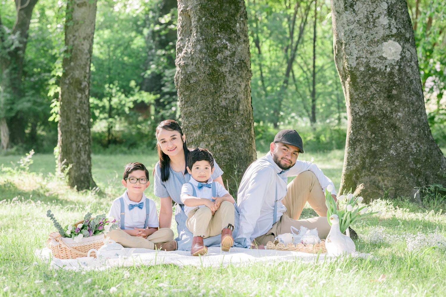 Family of four sitting on a blanket in a lush green park, posing for a portrait outdoors.