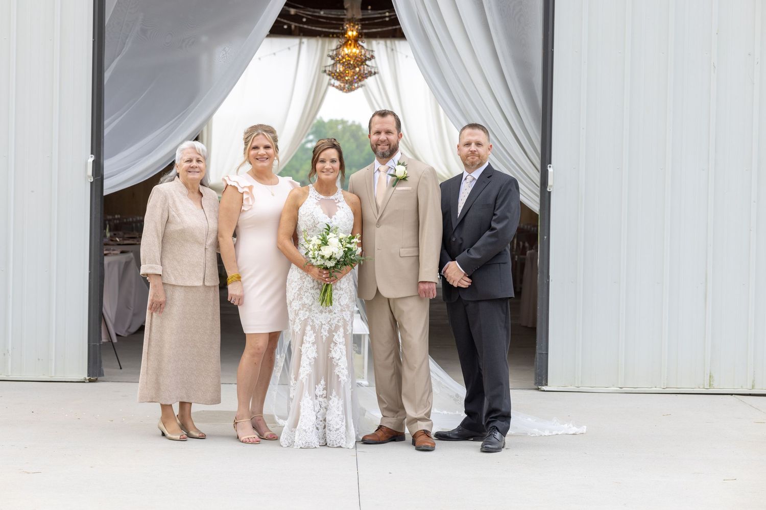Wedding party of five posing elegantly in neutral tones at a decorated venue entrance with draped curtains.