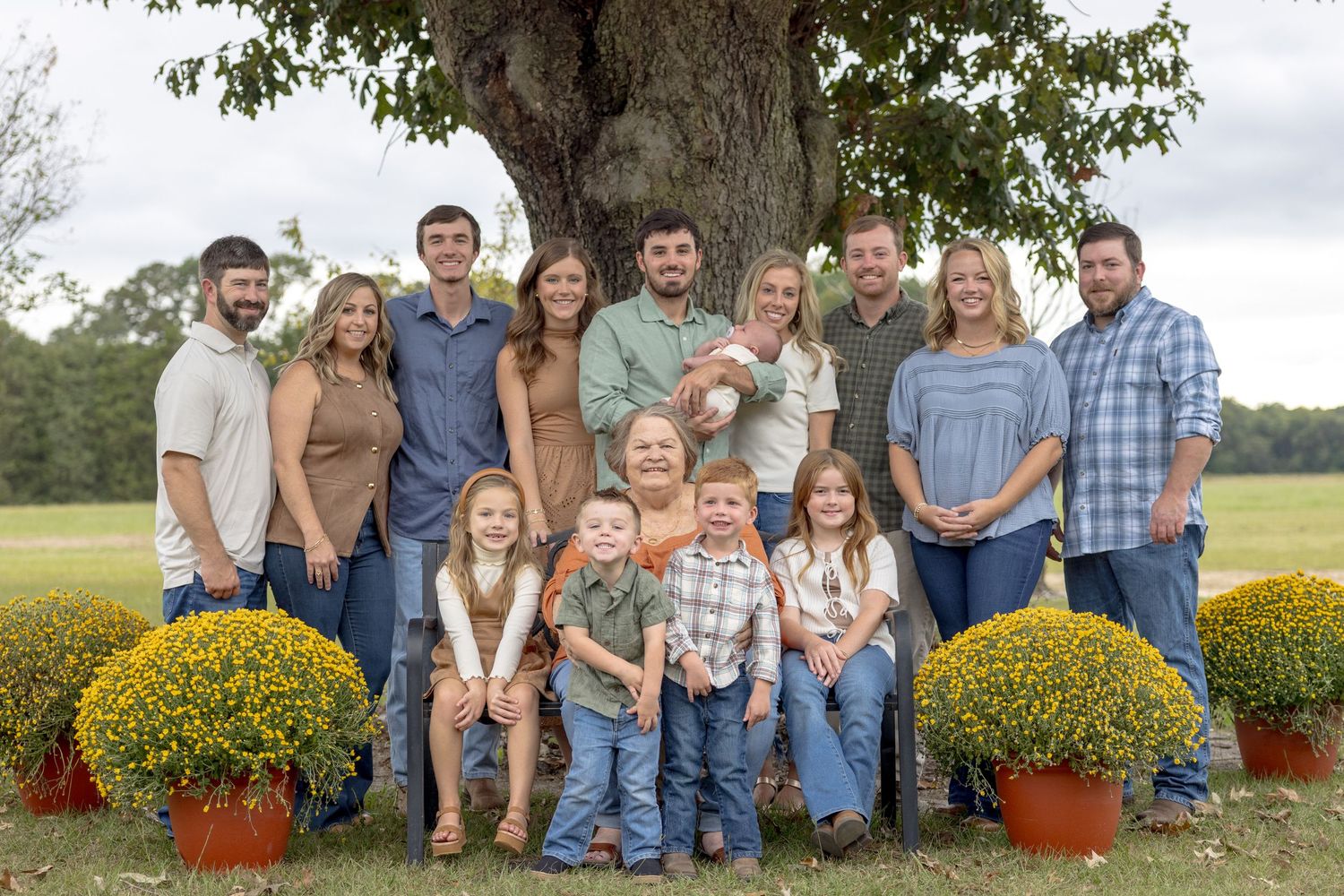 A large extended family poses together outdoors for a group portrait near autumn decorations.