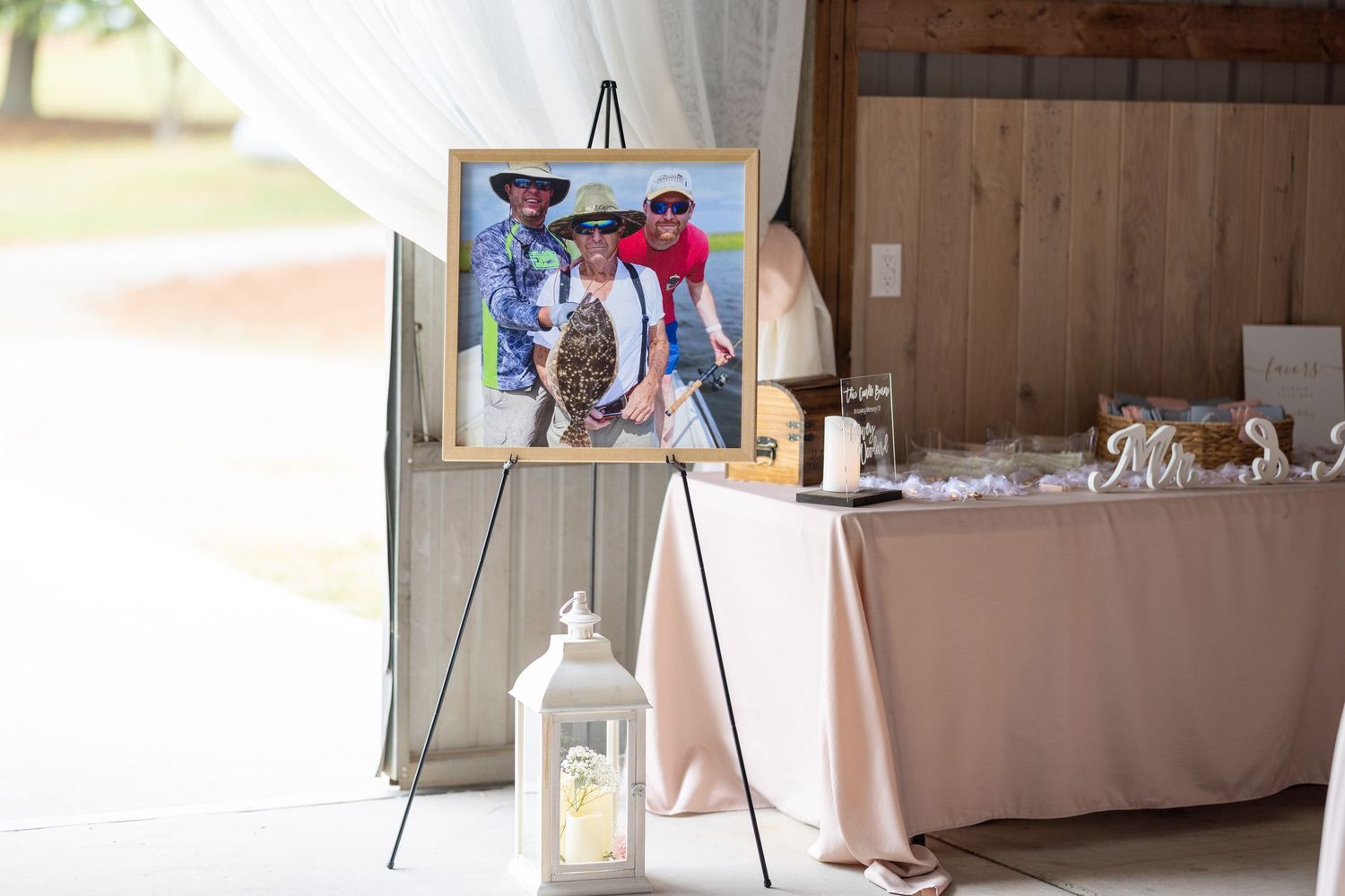 Framed family photo on easel display at elegant barn wedding reception with pink tablecloth and lanterns.