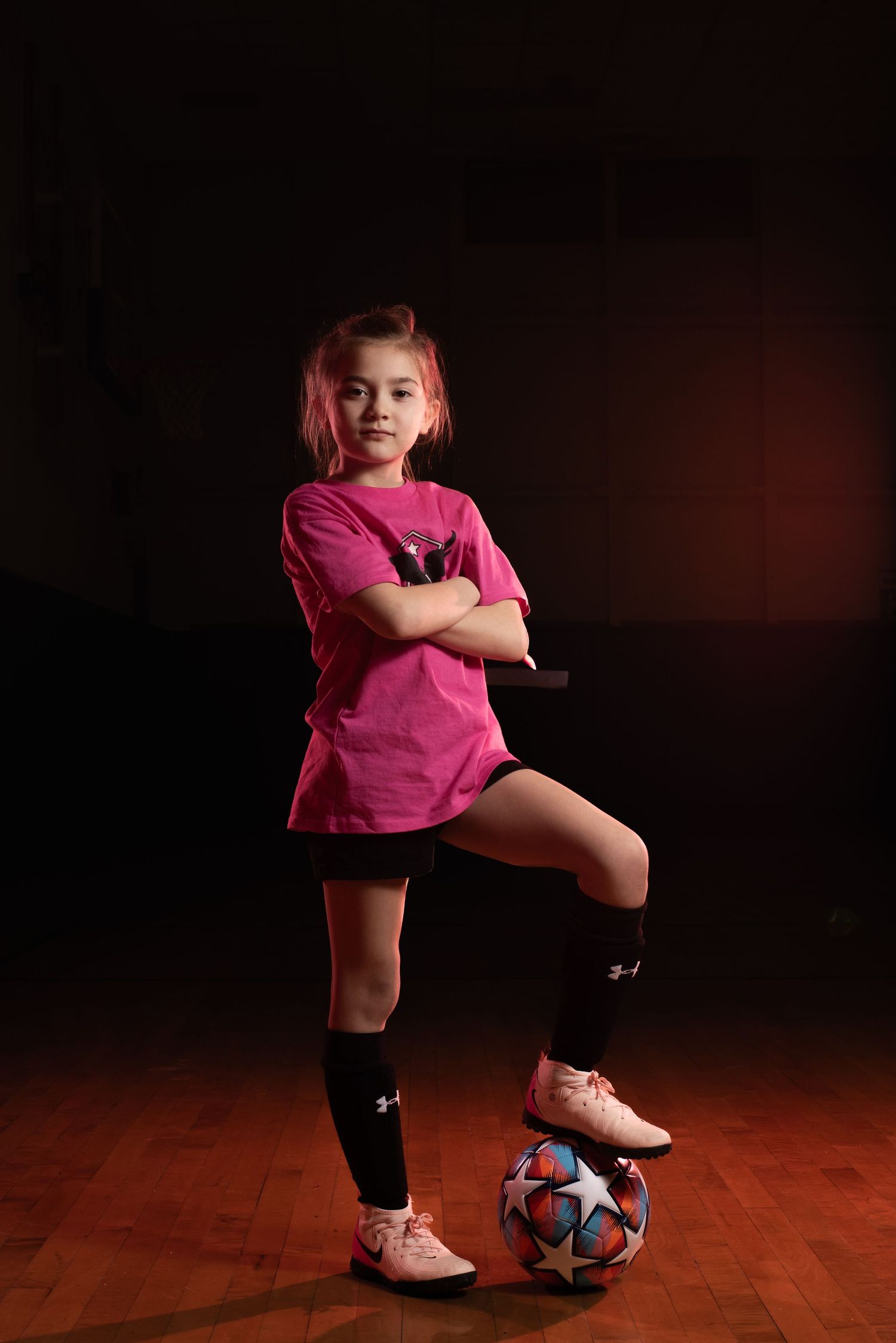 Soccer player in pink shirt stands with ball in dramatic studio portrait. Studio portrait of a youth athlete. Team photos.