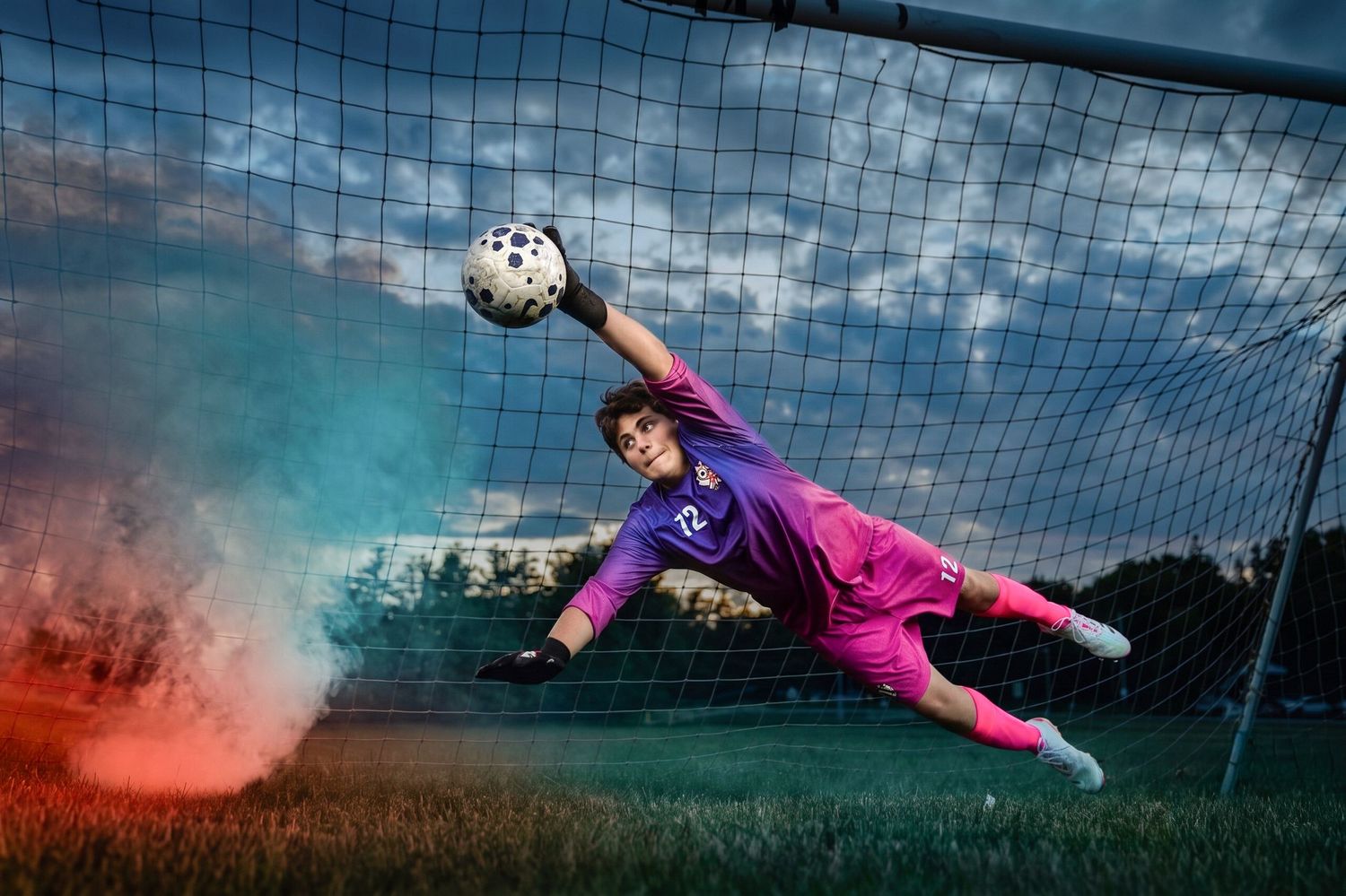 Soccer goalkeeper in purple uniform diving to block a ball near the net with colorful smoke effects at sunset.