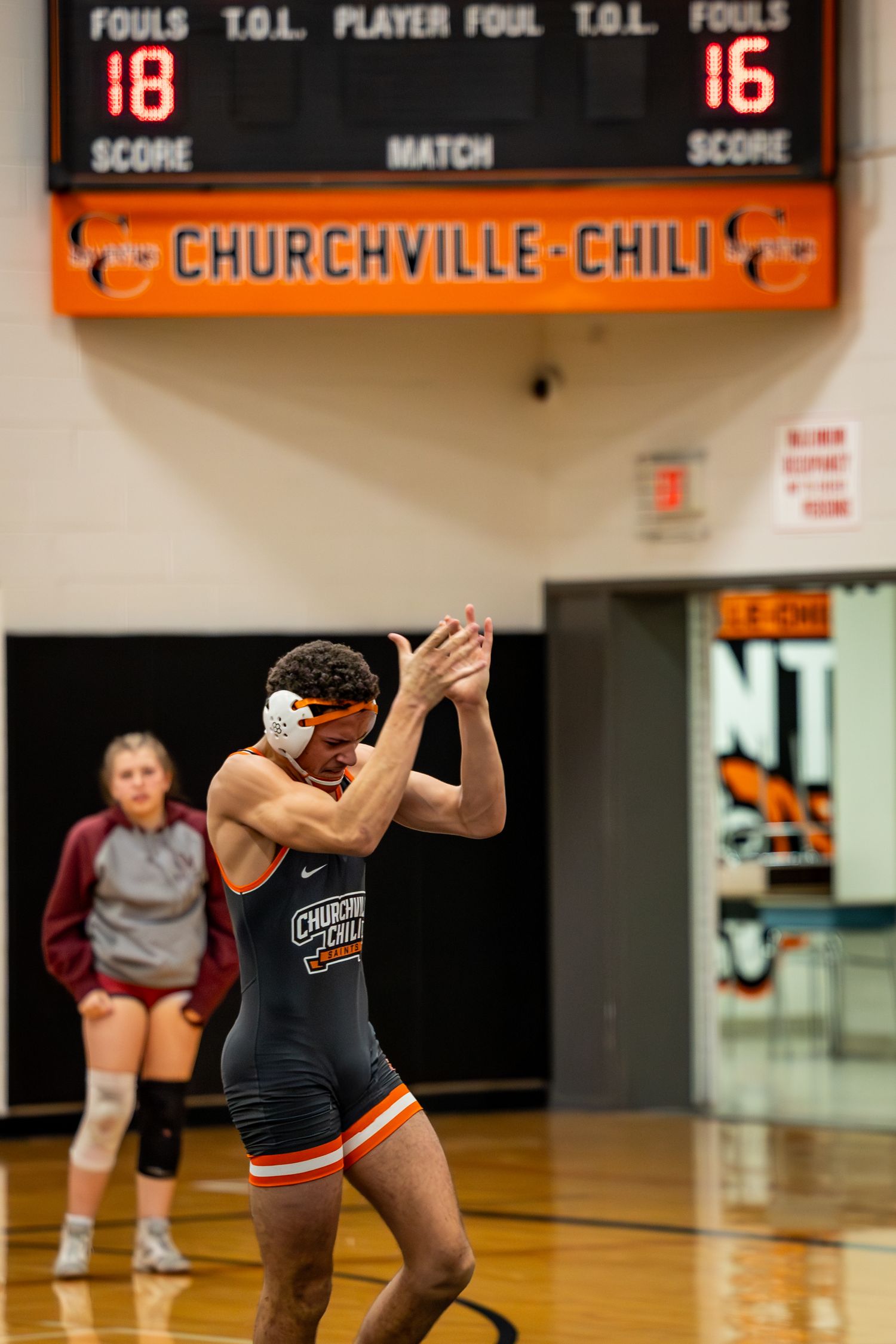 Wrestler in black uniform prepares for match under Churchville-Chili scoreboard. Studio portrait of a youth athlete. Team photos.