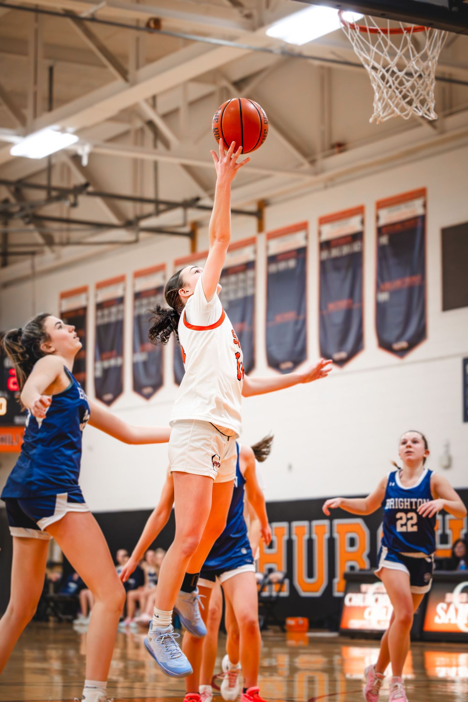 Basketball player reaches up to score during indoor game with opponents in blue jerseys. Studio portrait of a youth athlete. Team photos.