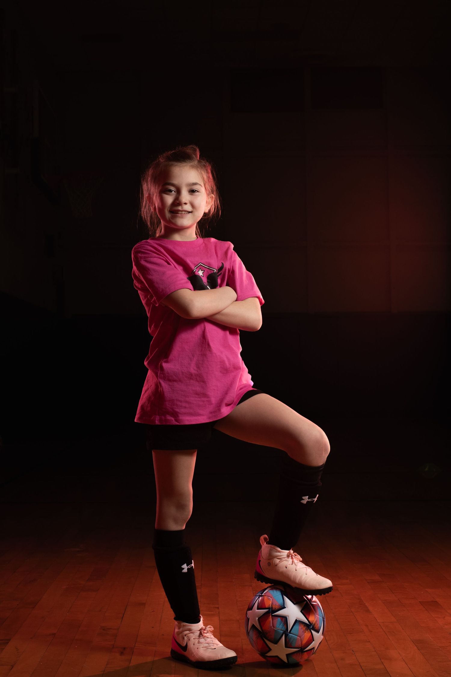 Young athlete practices soccer moves with ball against dark background in pink shirt. Studio portrait of a youth athlete. Team photos.