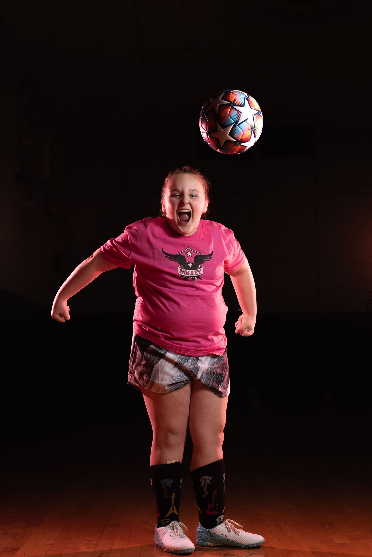 Young soccer player in pink shirt practices ball control skills against dark background. Studio portrait of a youth athlete. Team photos.