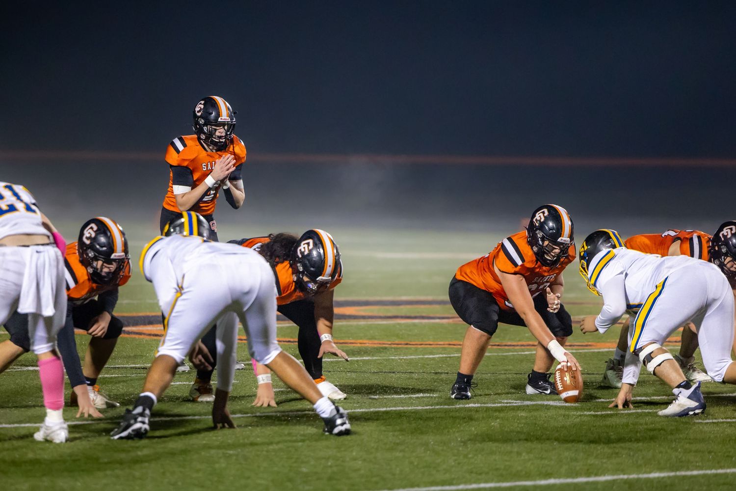 Football teams line up at scrimmage during nighttime game on illuminated field. Studio portrait of a youth athlete. Team photos.