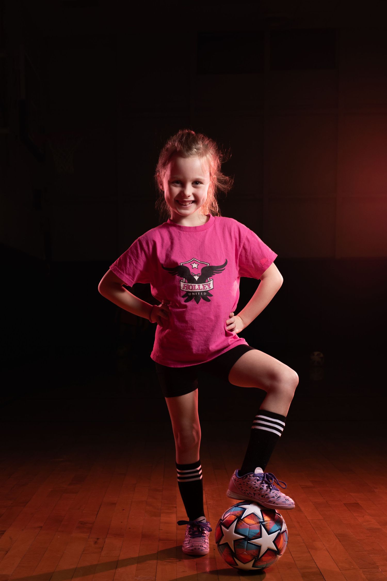 Young athlete strikes confident pose with soccer ball in studio with red lighting. Studio portrait of a youth athlete. Team photos.