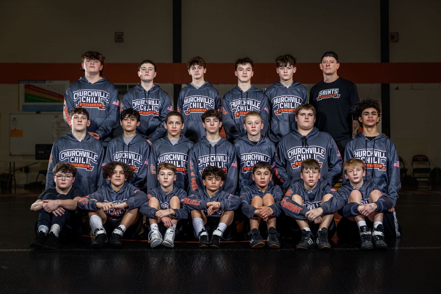 High school wrestling team poses for group photo in matching gray Churchill team sweatshirts in gymnasium.