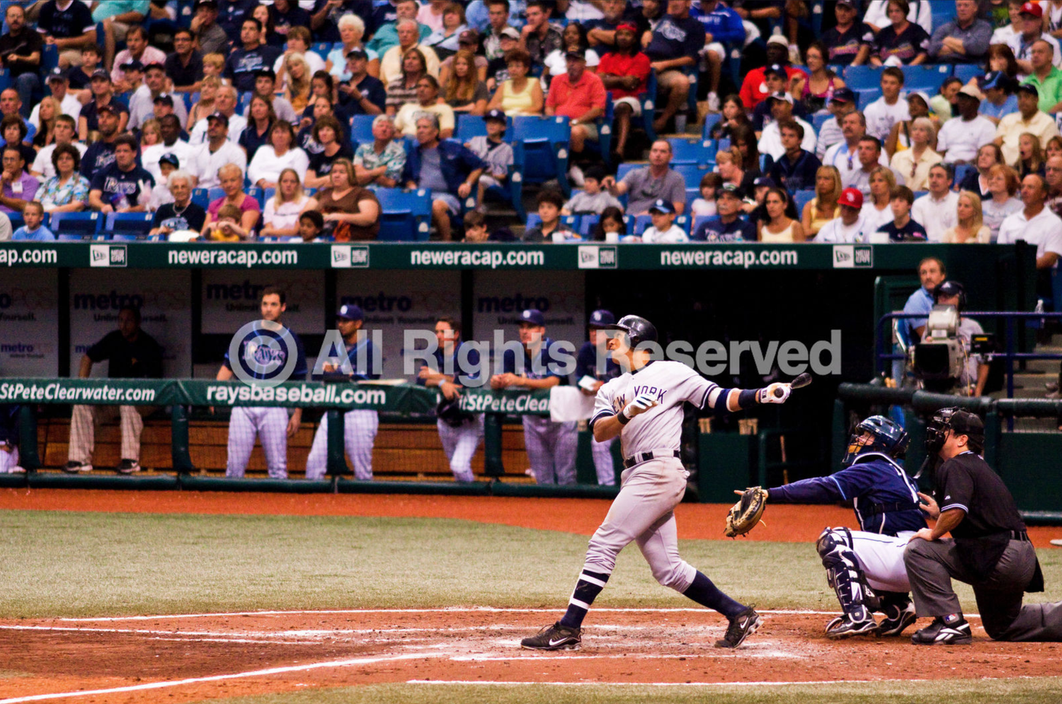 A baseball batter takes a swing at home plate during a professional game at Tropicana Field with fans in the background.