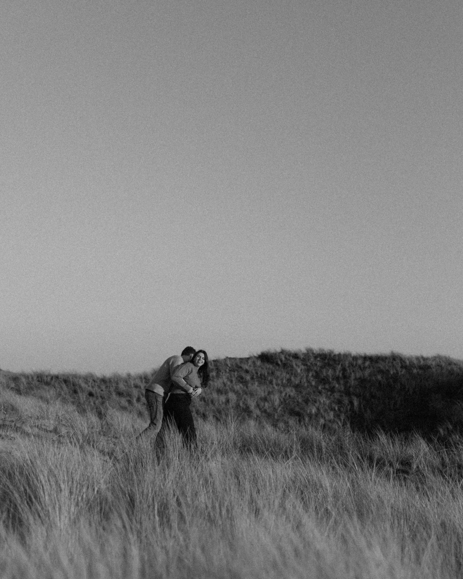 Two figures standing close together in tall grass against a grey sky.