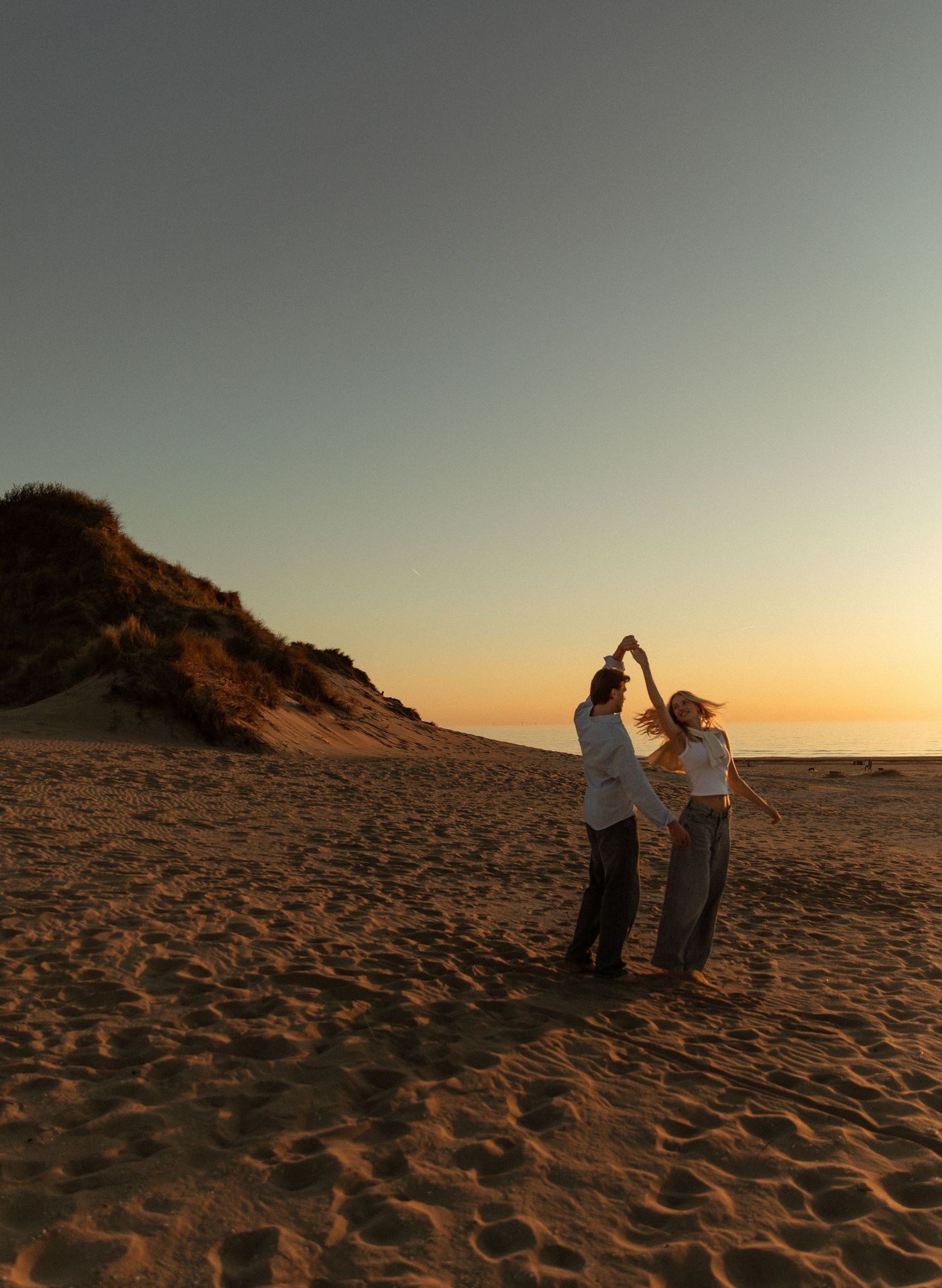 Two people dancing on a sandy beach at golden sunset with sand dunes in the background.